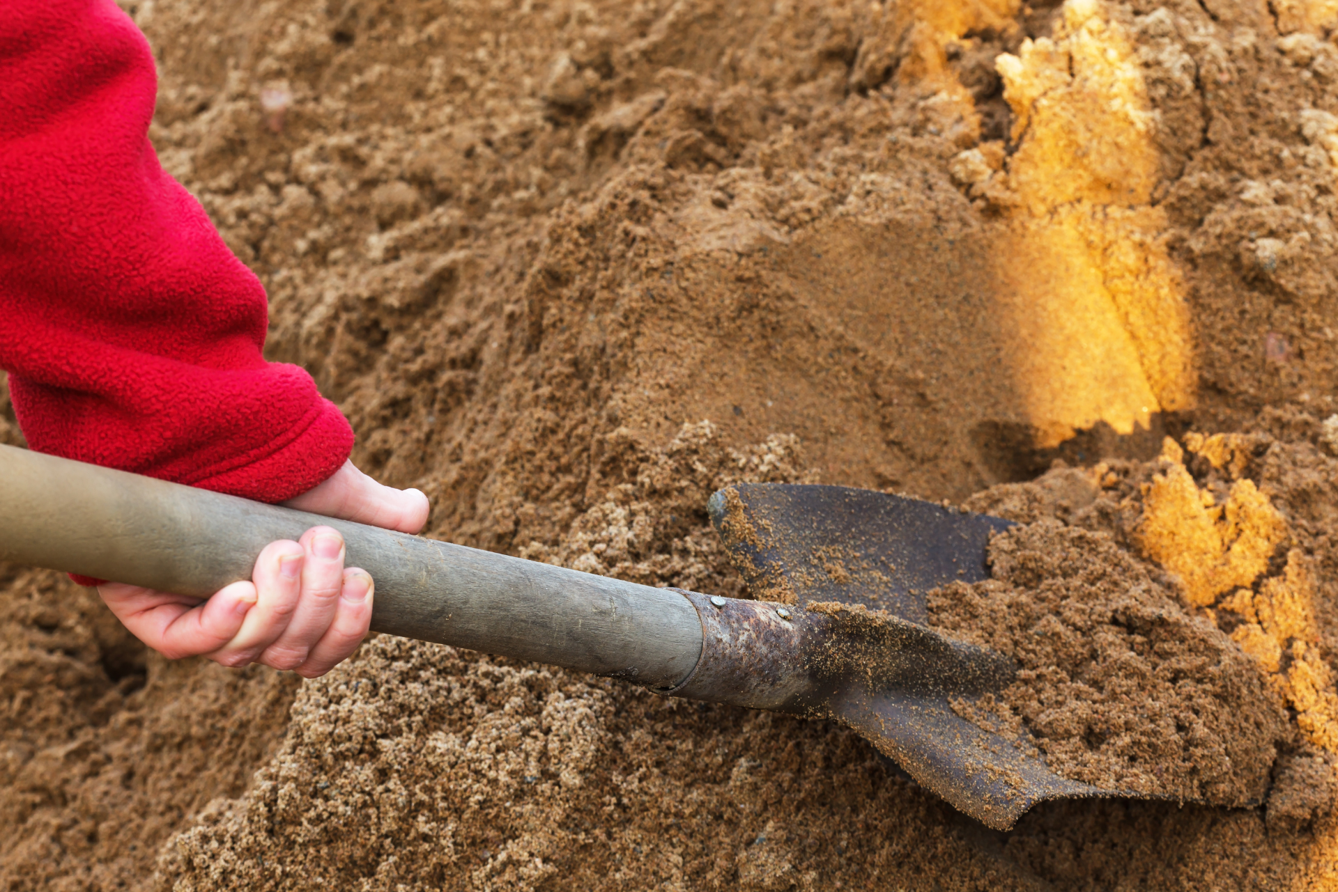 Eine Person gräbt mit einer Schaufel im Sand.