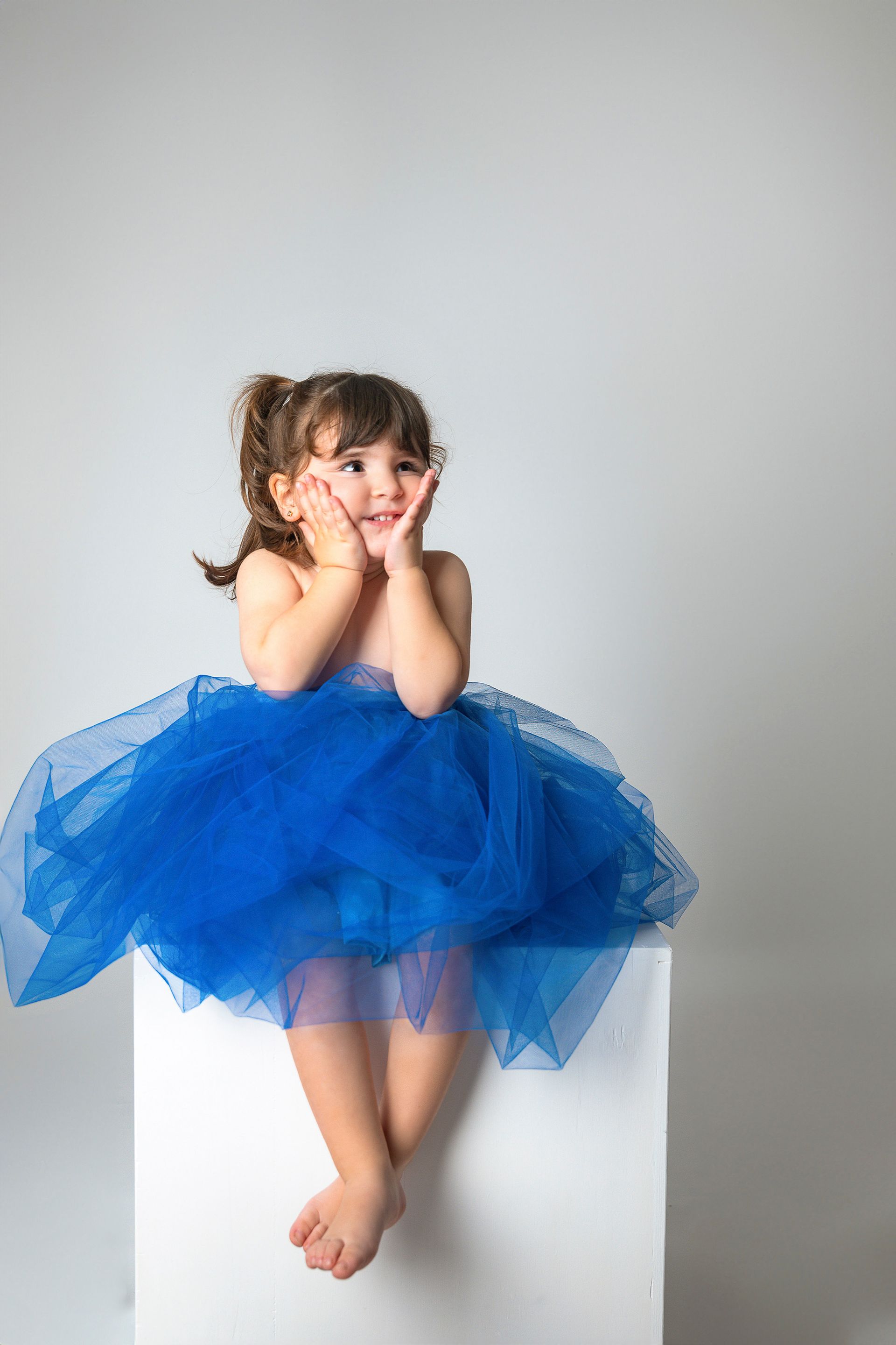 Una niña con un tutú azul está sentada en un cubo blanco.