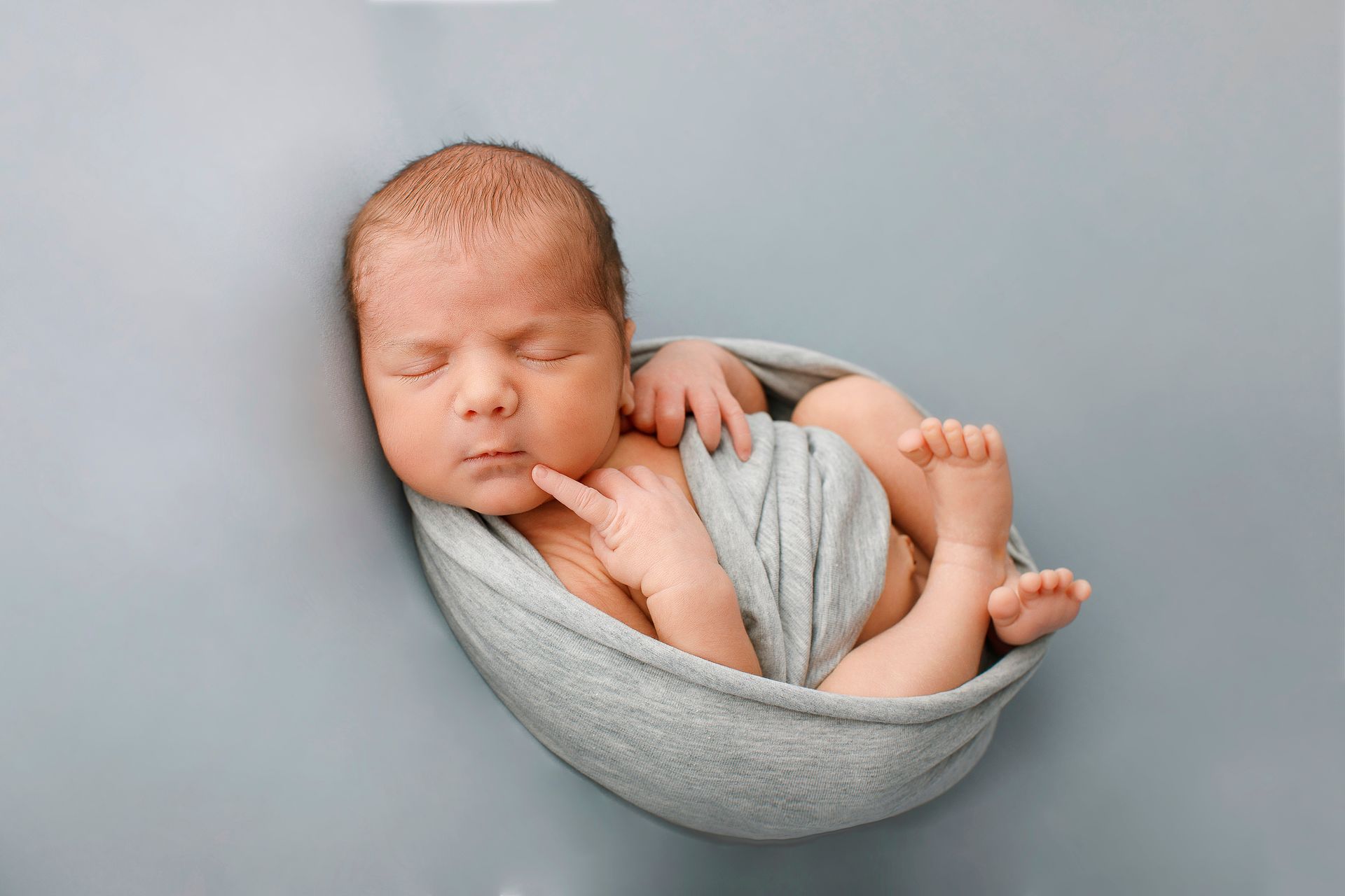 Un bebé recién nacido duerme en una manta gris.