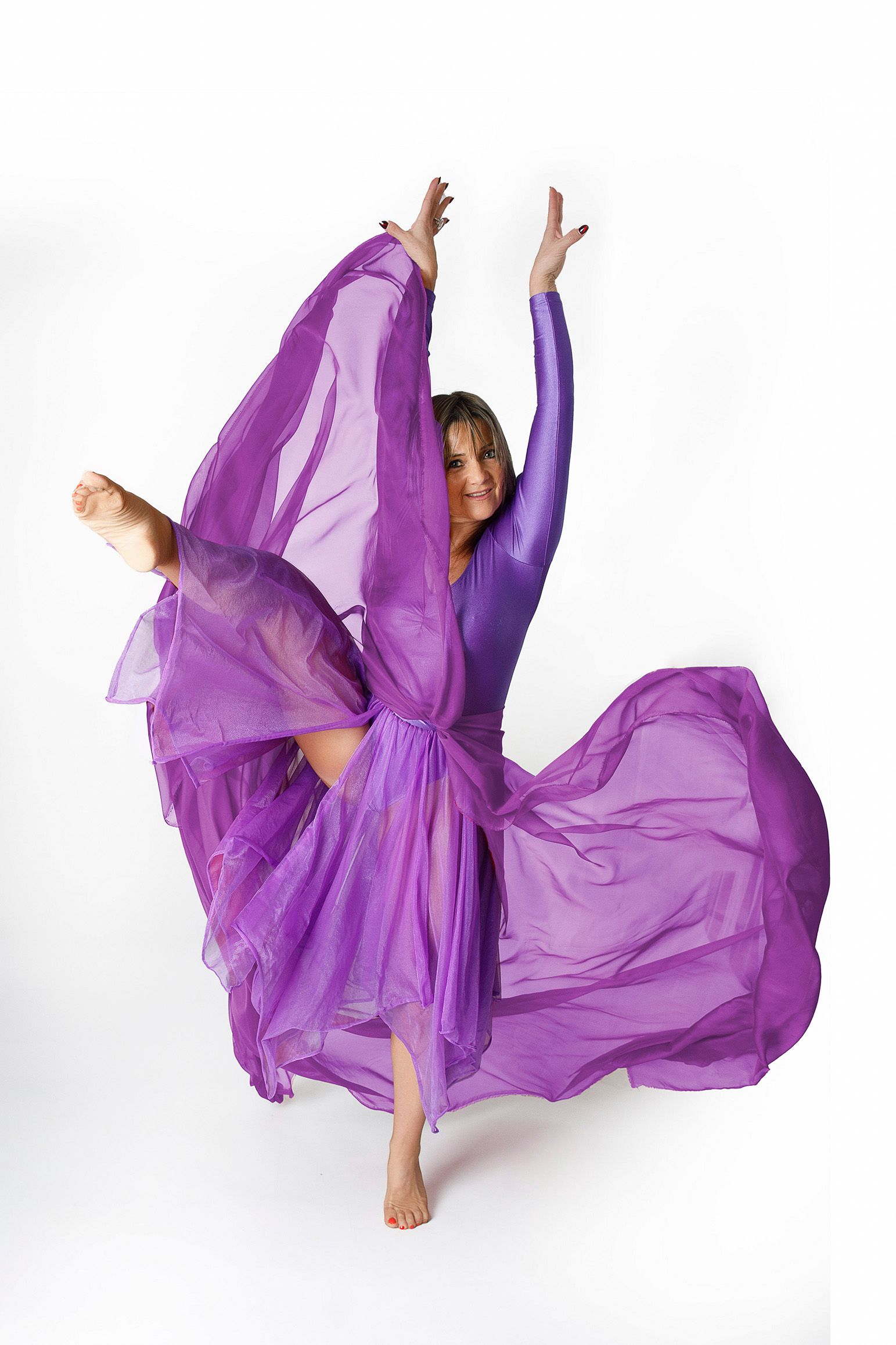 Una mujer con un vestido morado está bailando con los brazos en el aire.