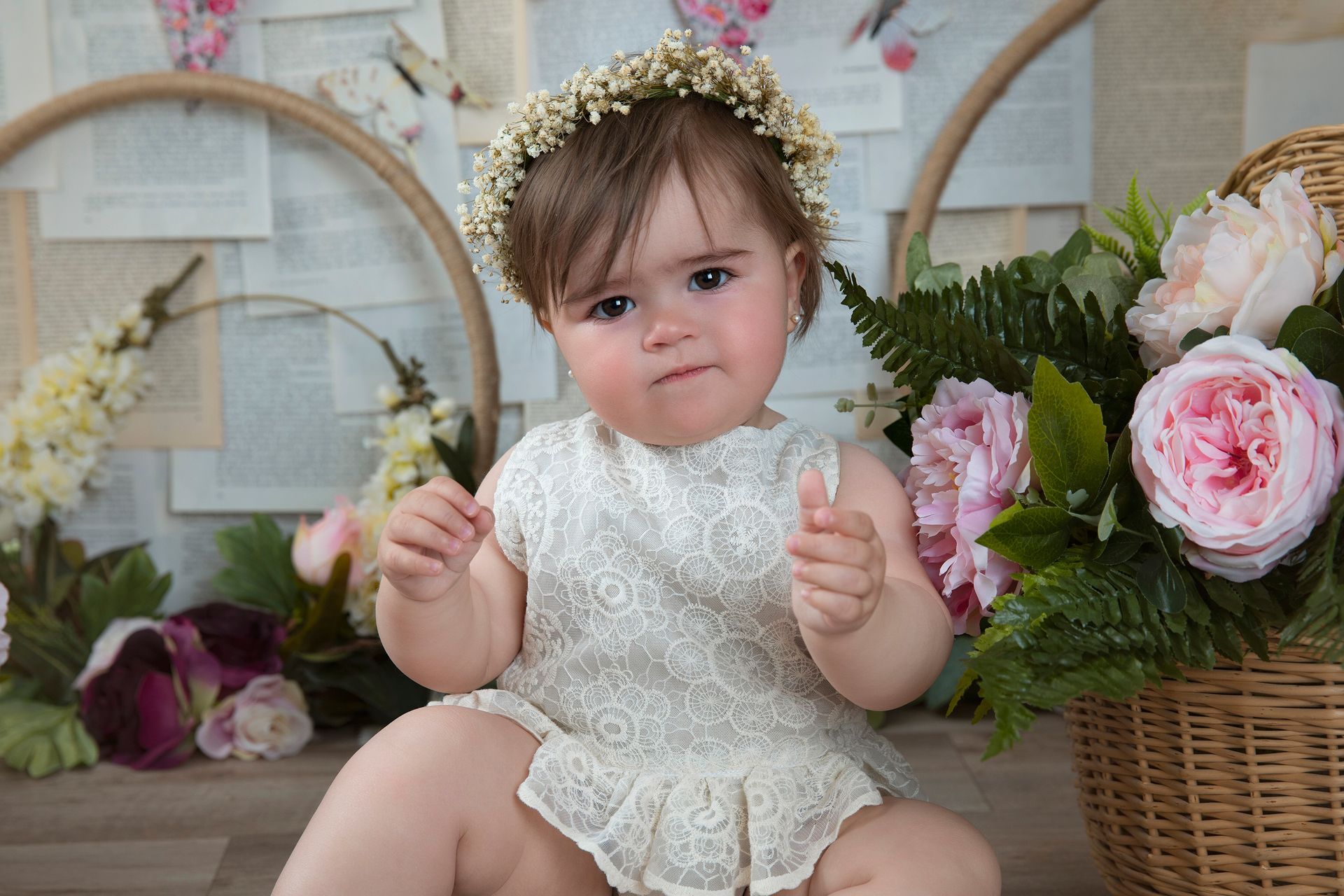 Una niña que lleva una corona de flores está sentada junto a una canasta de flores.