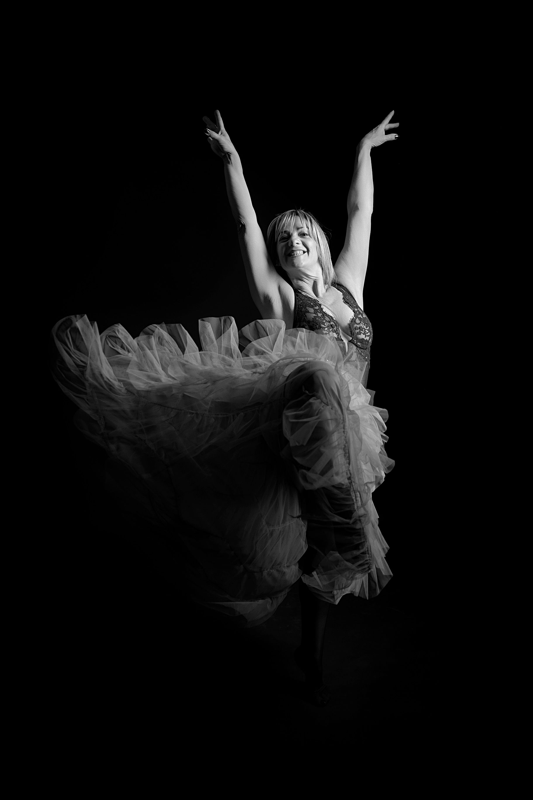 Una fotografía en blanco y negro de una mujer con un vestido bailando con los brazos en el aire.