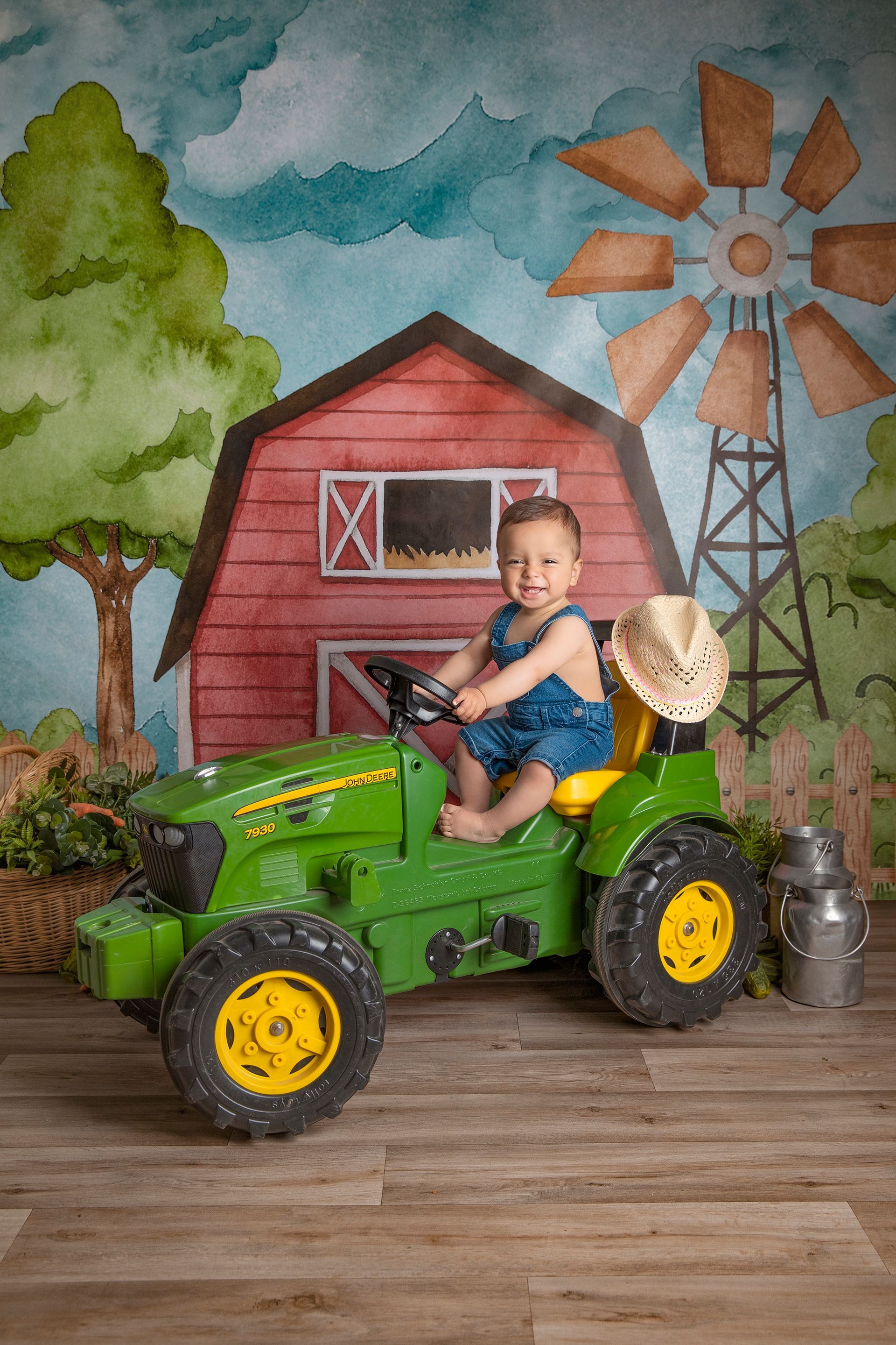 Un bebé está sentado en un tractor de juguete frente a un granero y un molino de viento.