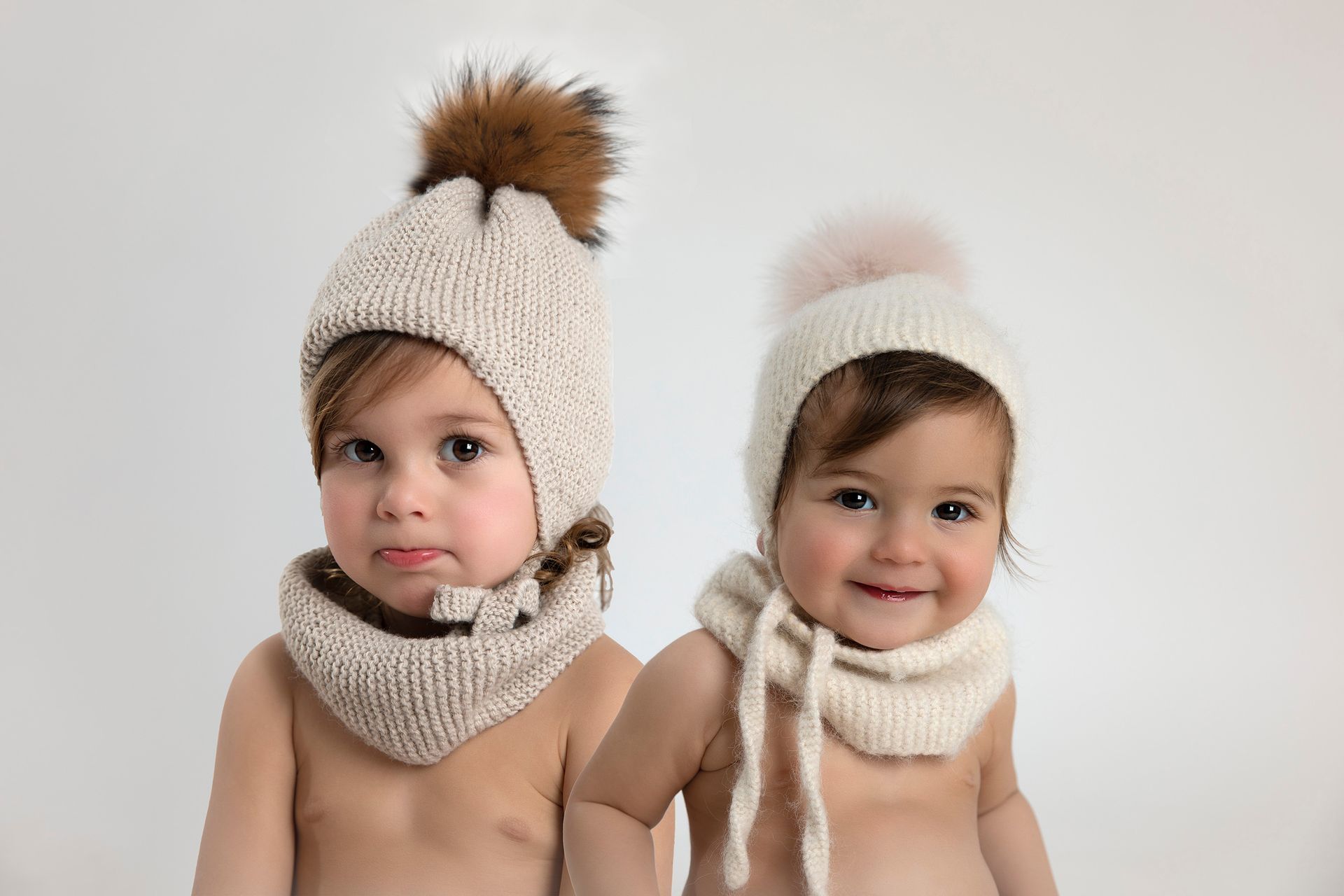 Dos bebés que llevan gorros y bufandas de punto están parados uno al lado del otro.