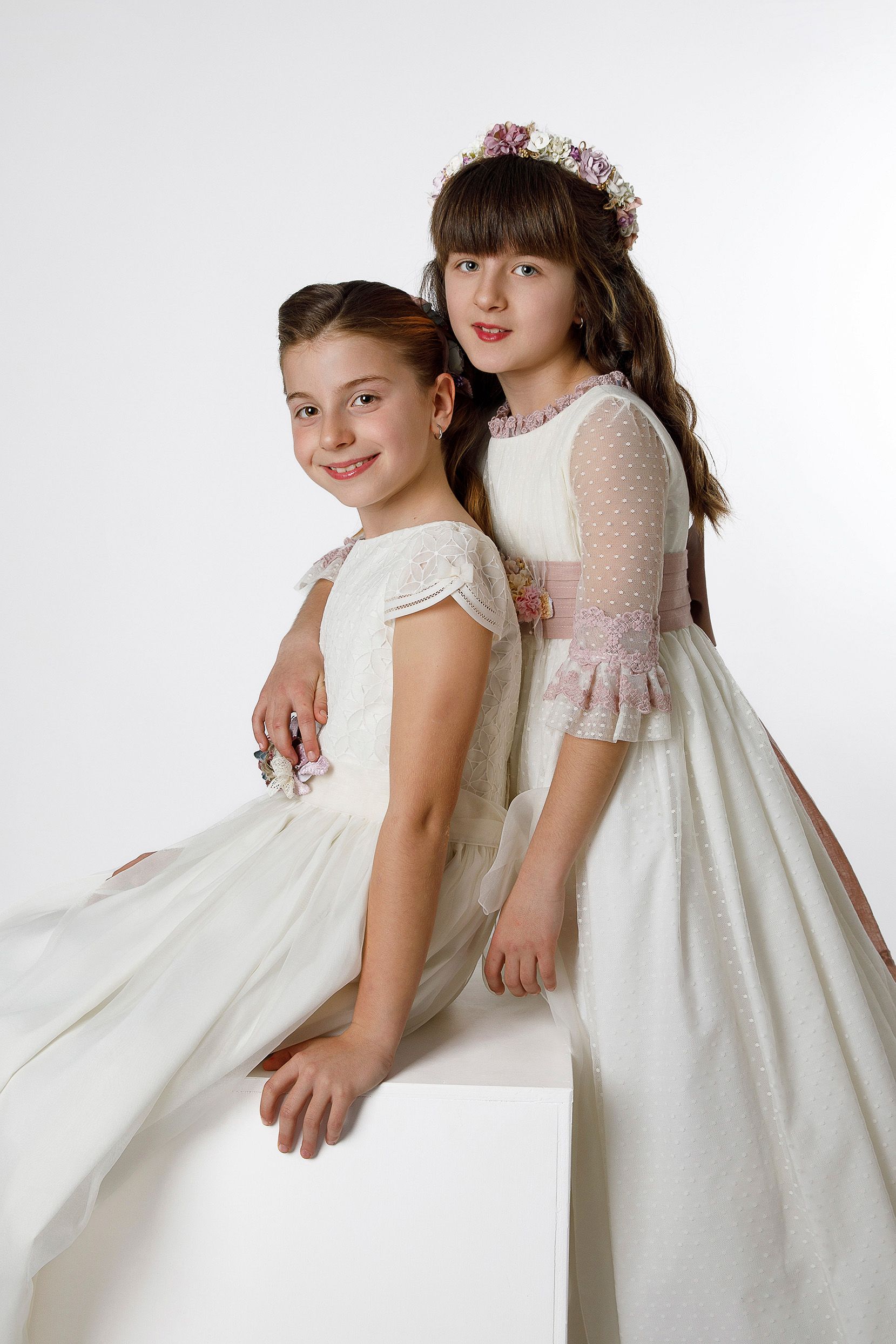 Dos niñas con vestidos blancos están sentadas en un cubo blanco.