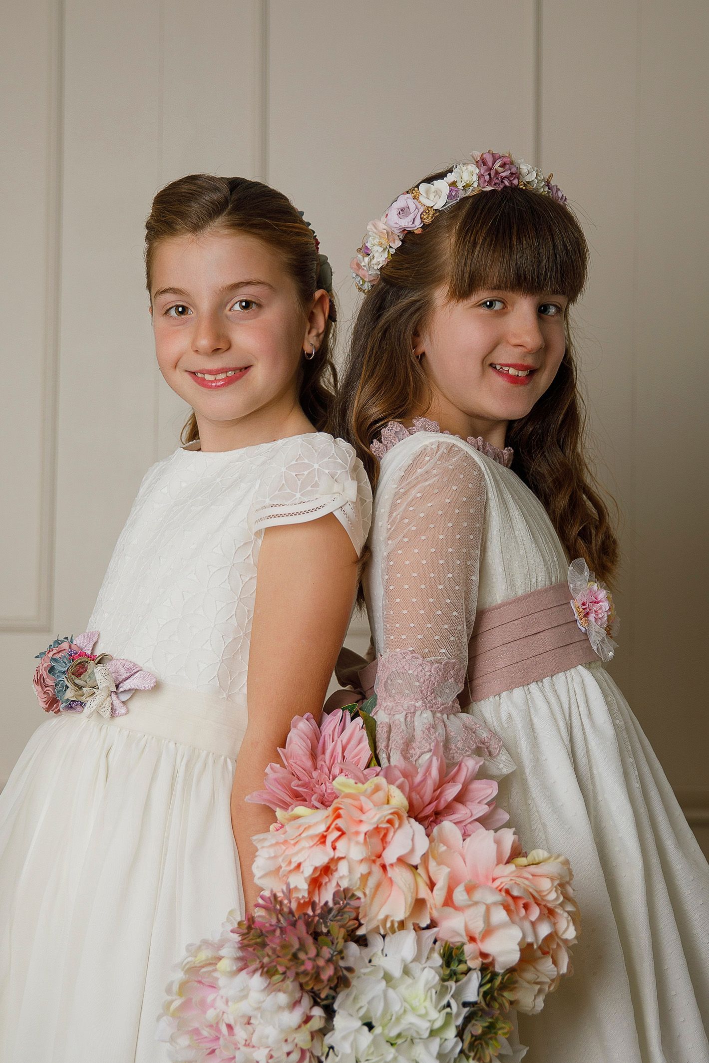 Dos niñas con vestidos blancos están paradas una al lado de la otra sosteniendo flores.
