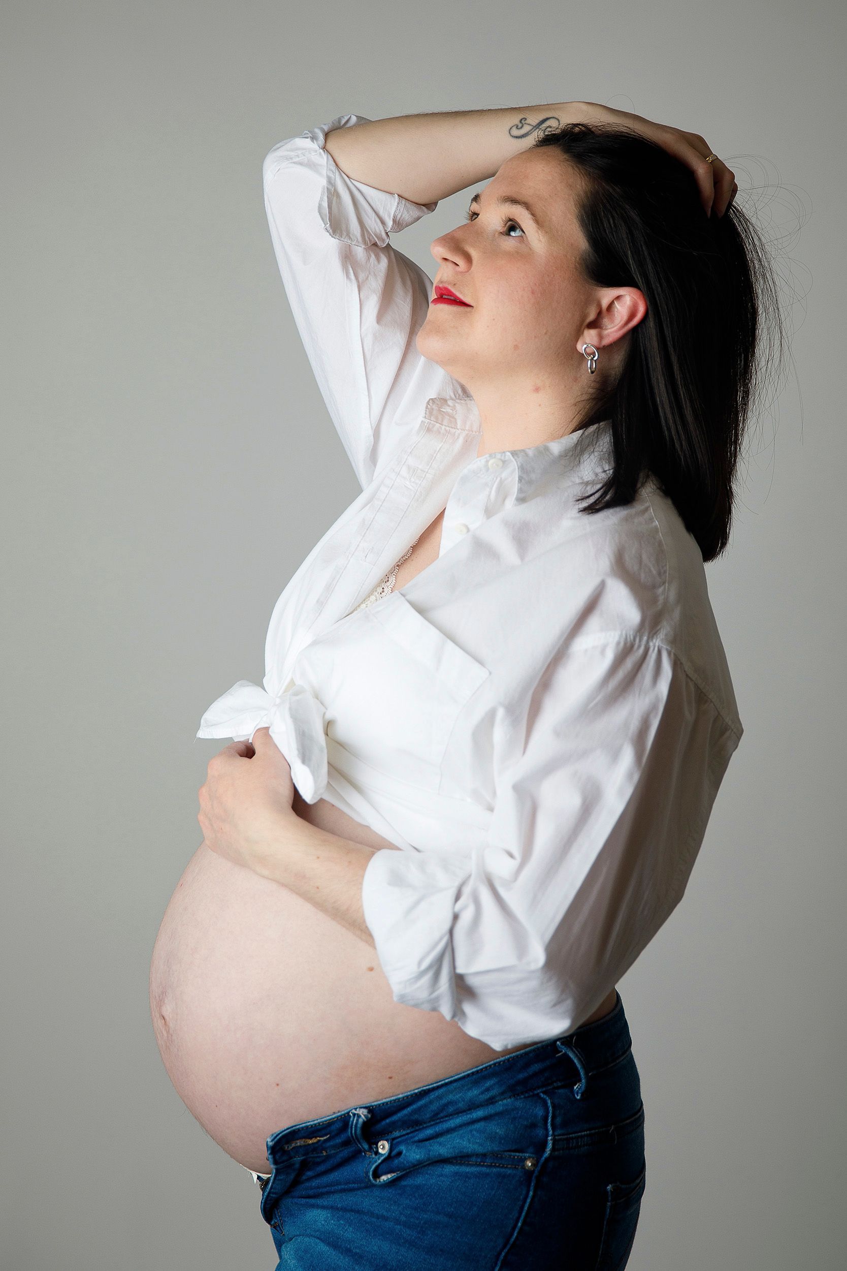 Una mujer embarazada con una camisa blanca y jeans azules sostiene su vientre.