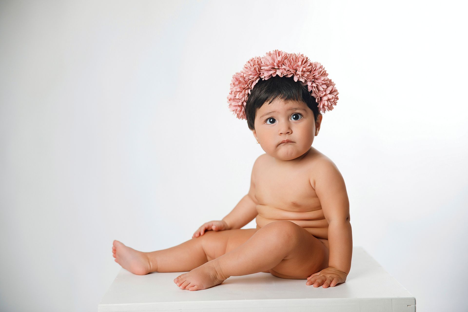 Un bebé que lleva una corona de flores está sentado en una caja blanca.