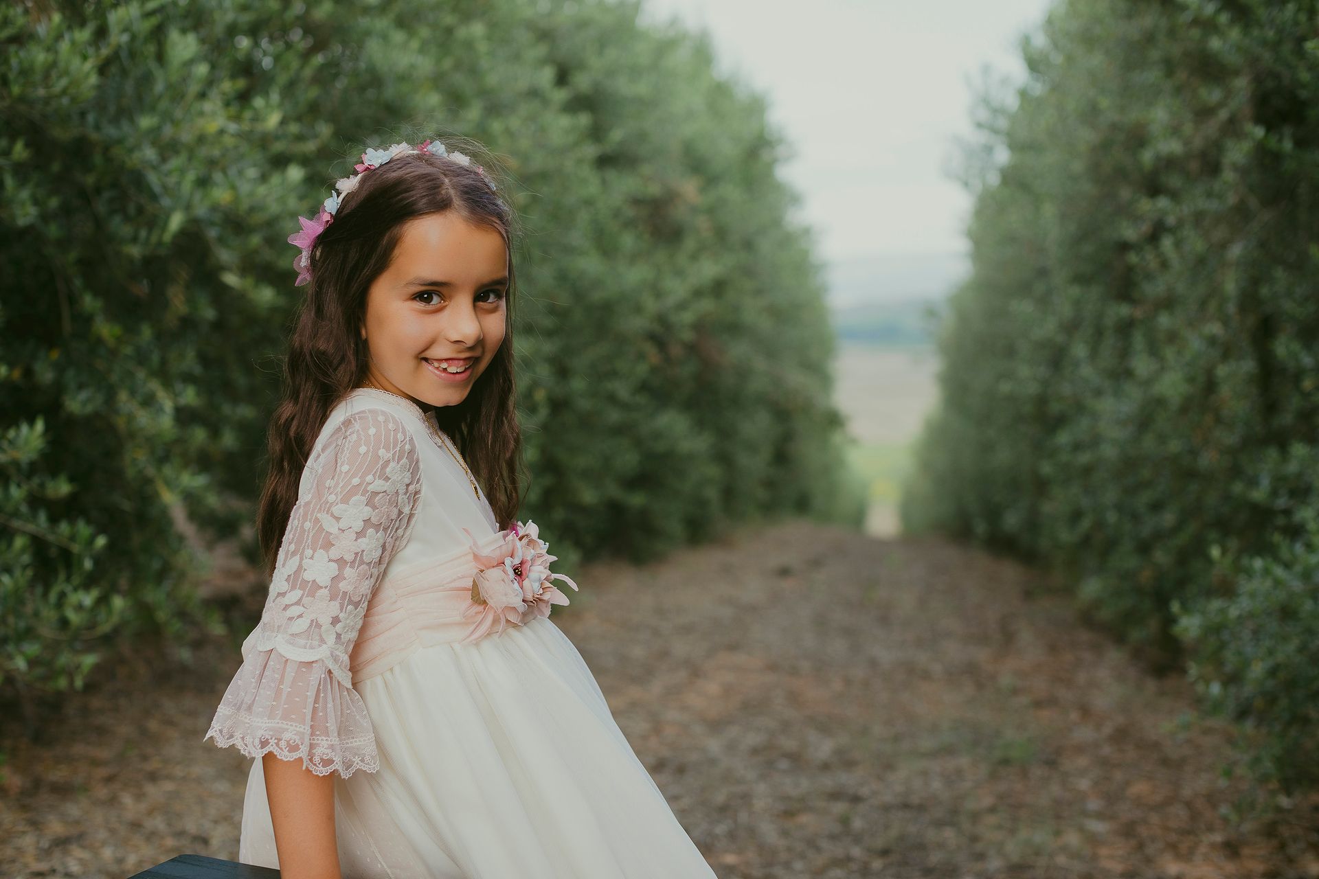 Una niña con un vestido blanco está sentada en un banco en un bosque.