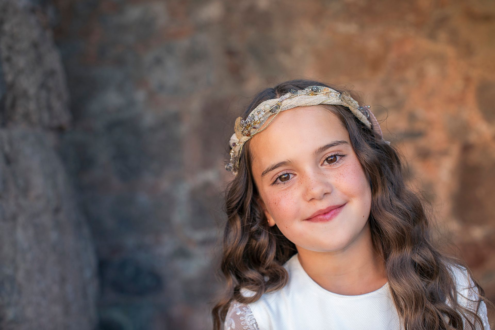 Una niña que lleva una diadema y un vestido blanco sonríe para la cámara.