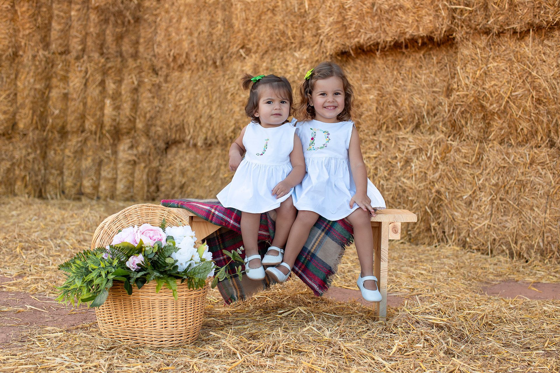 Dos niñas están sentadas en un banco frente a un fardo de heno.