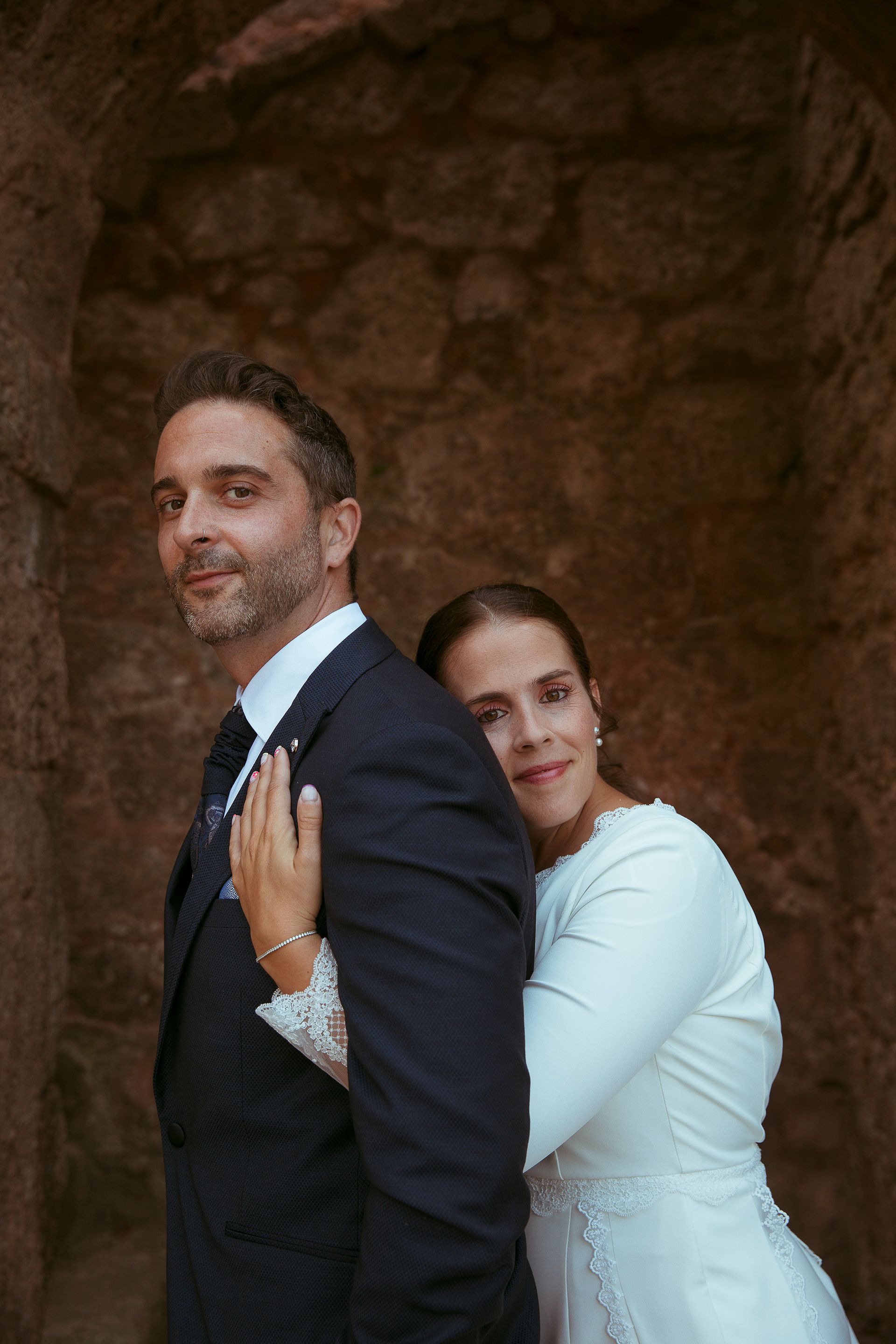 Una novia y un novio posan para una foto frente a un muro de piedra.