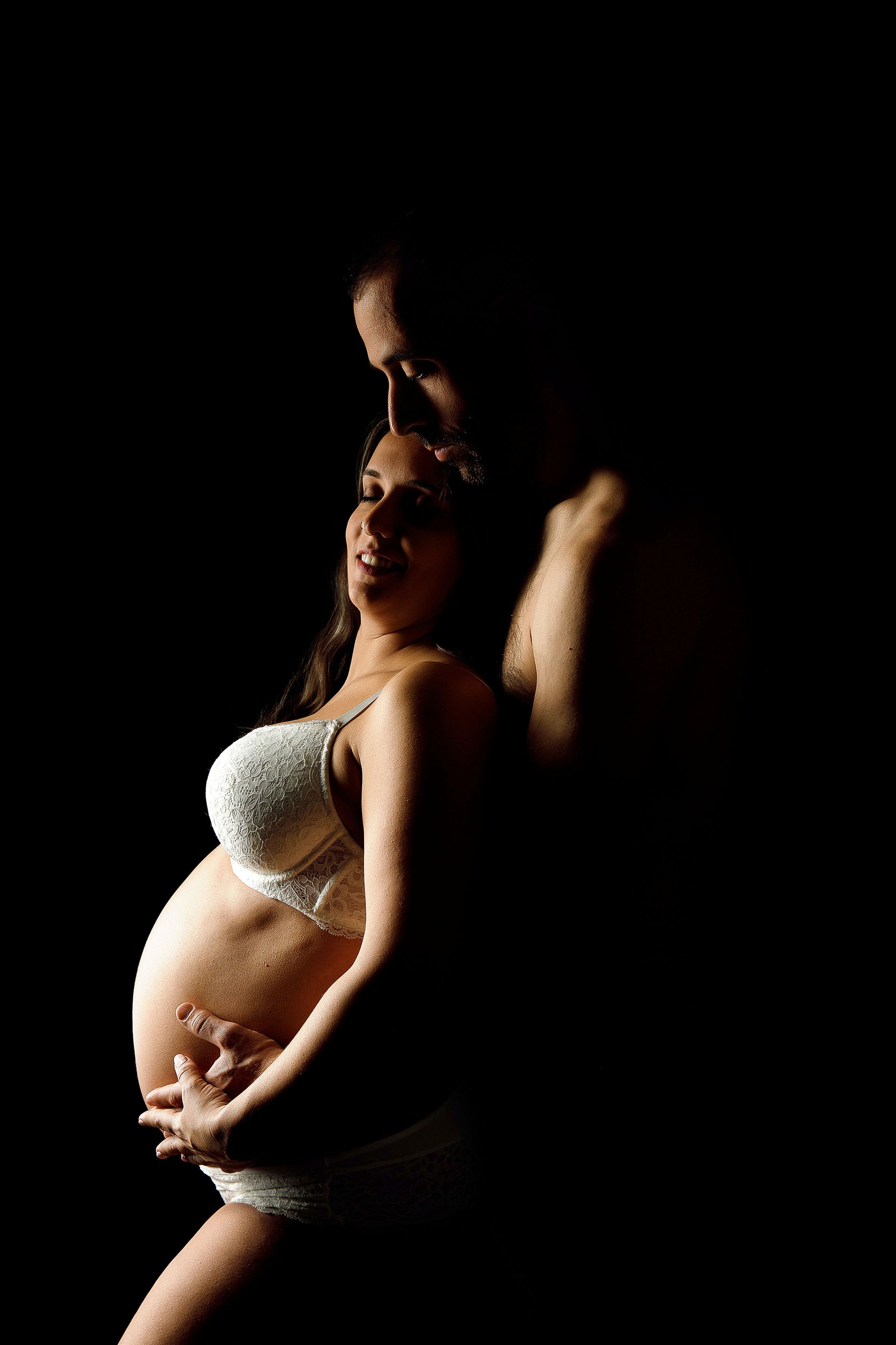 Un hombre y una mujer embarazada se abrazan en la oscuridad.