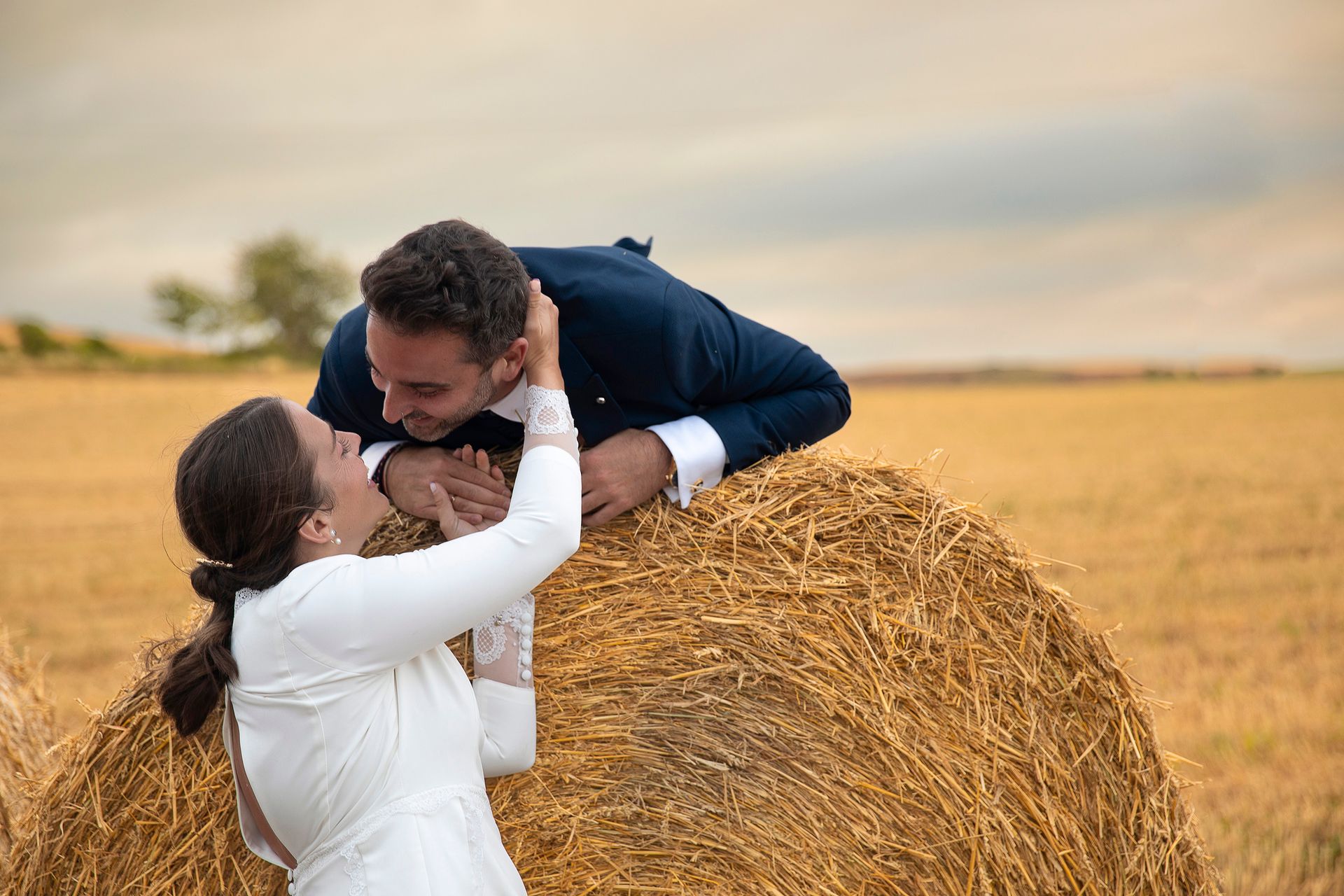 Una novia y un novio se besan encima de un fardo de heno.