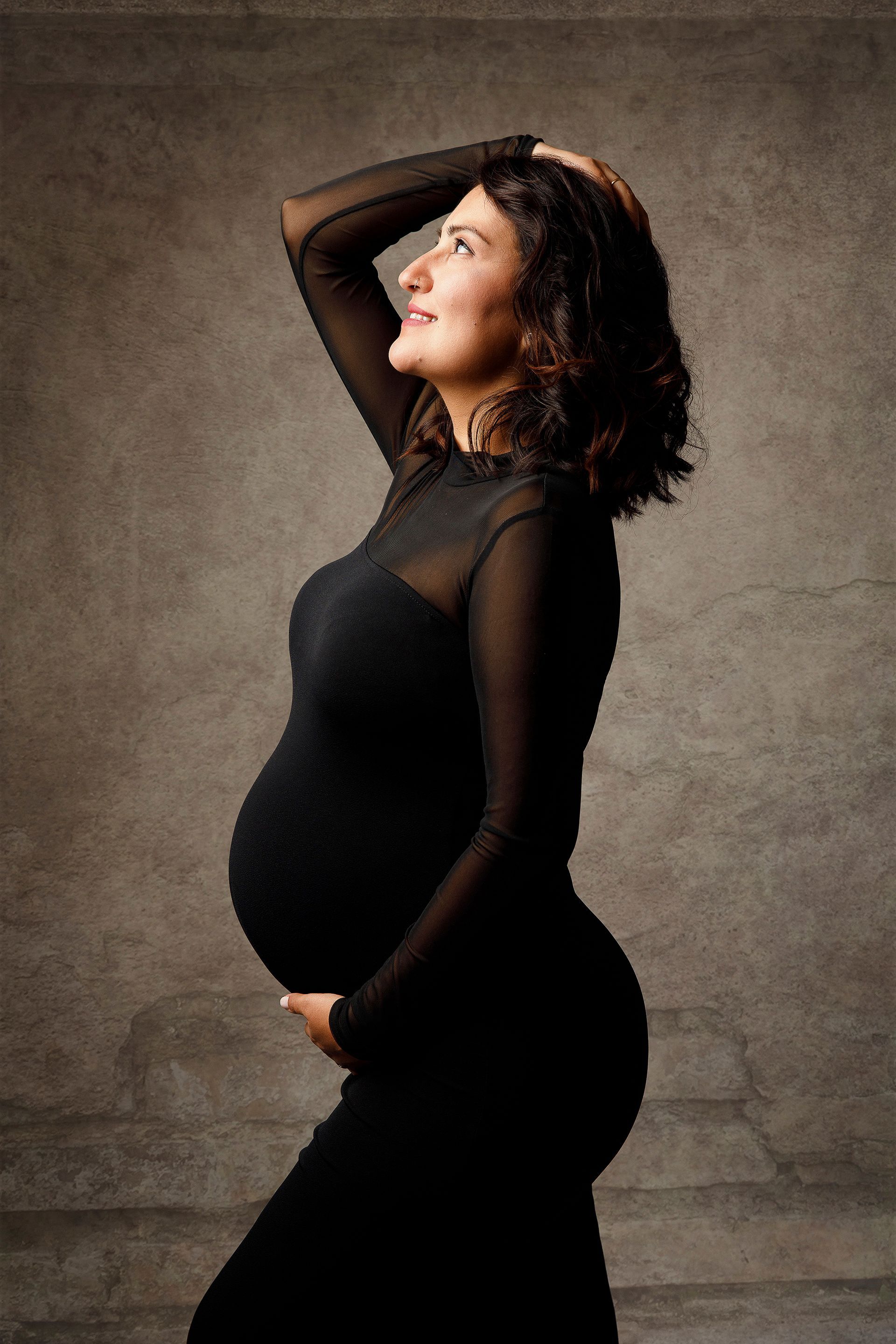 Una mujer embarazada lleva un vestido negro y sostiene su vientre.