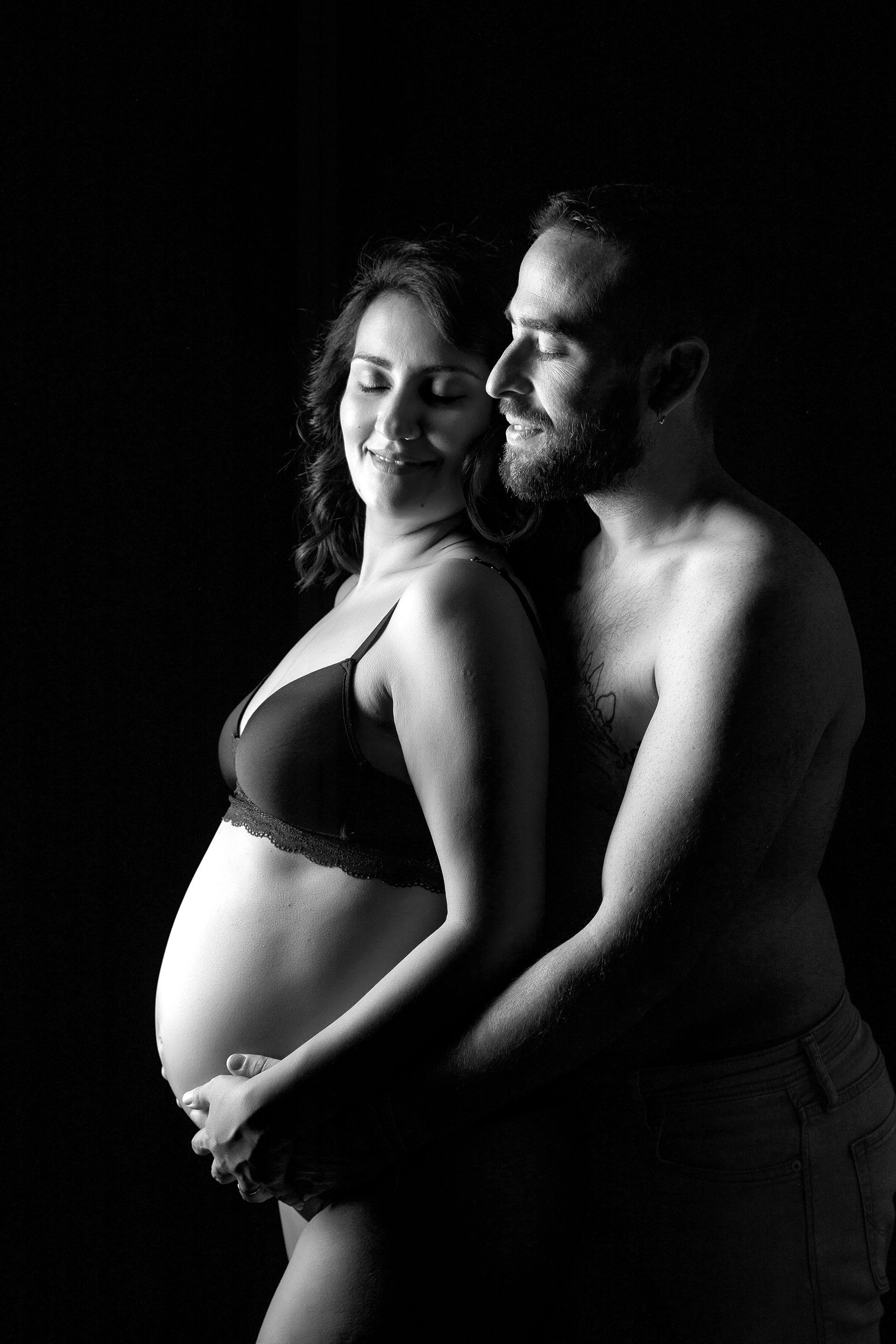 Un hombre y una mujer embarazada posan para una fotografía en blanco y negro.