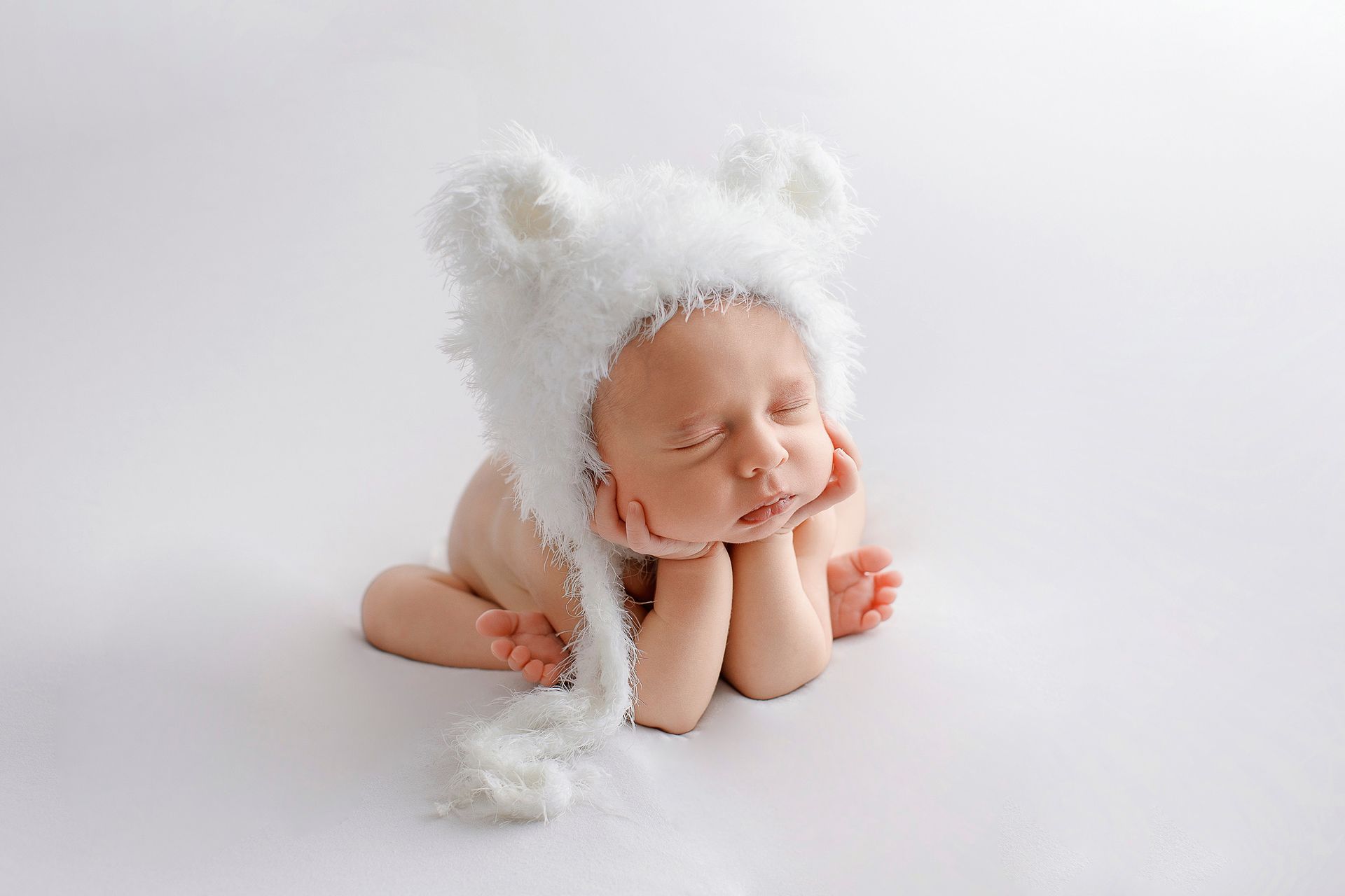 Un bebé recién nacido que lleva un sombrero blanco con orejas está durmiendo.