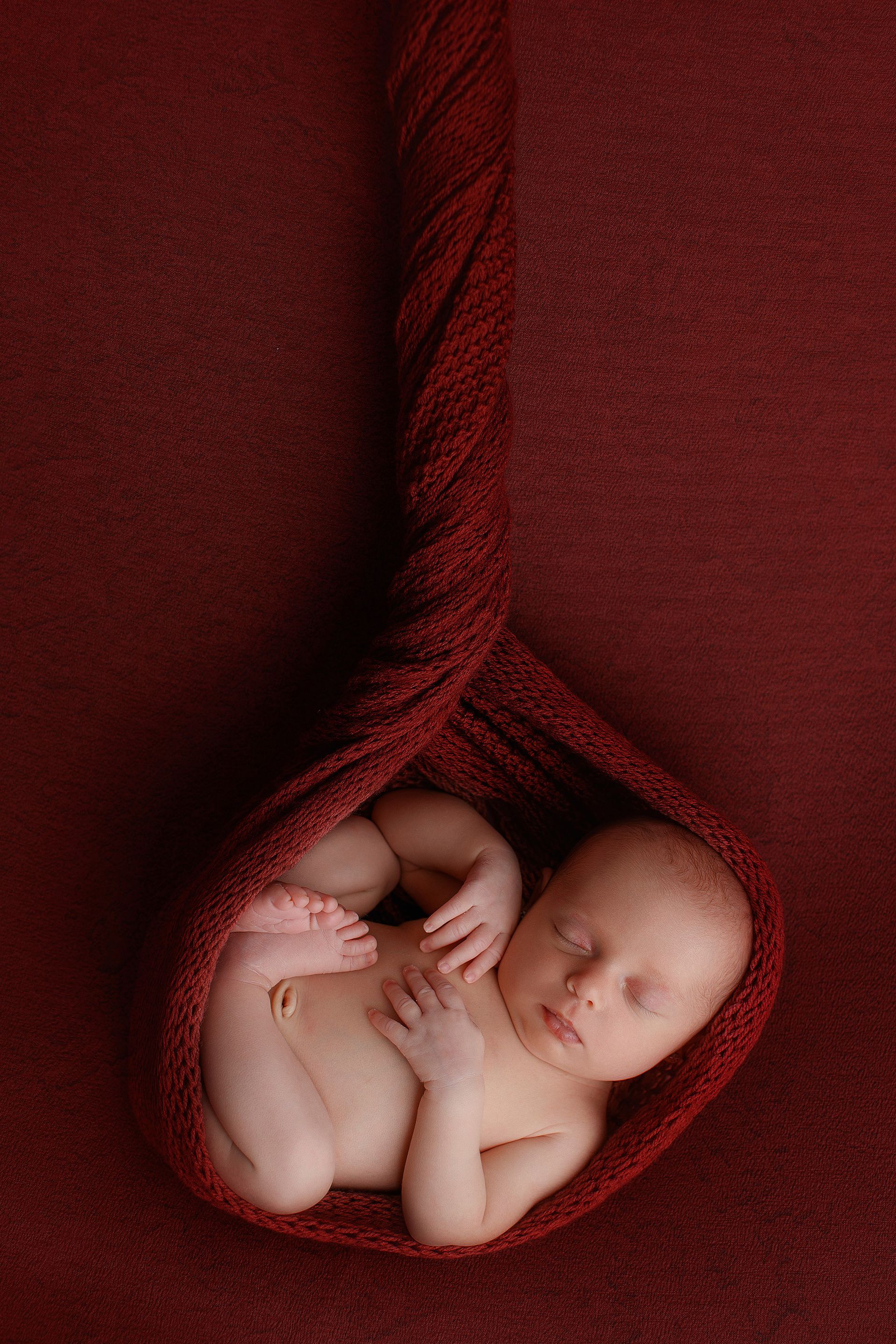 Un bebé recién nacido está envuelto en una manta roja.