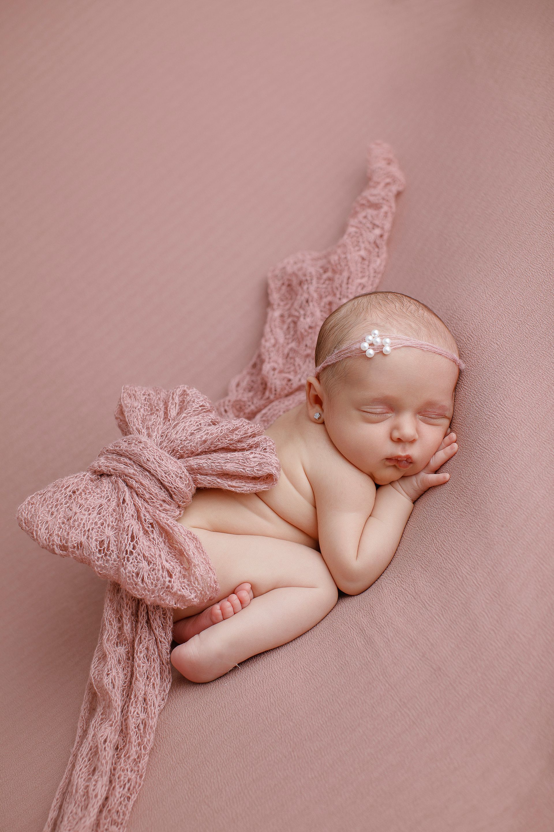 Una niña recién nacida está durmiendo sobre una manta rosa.