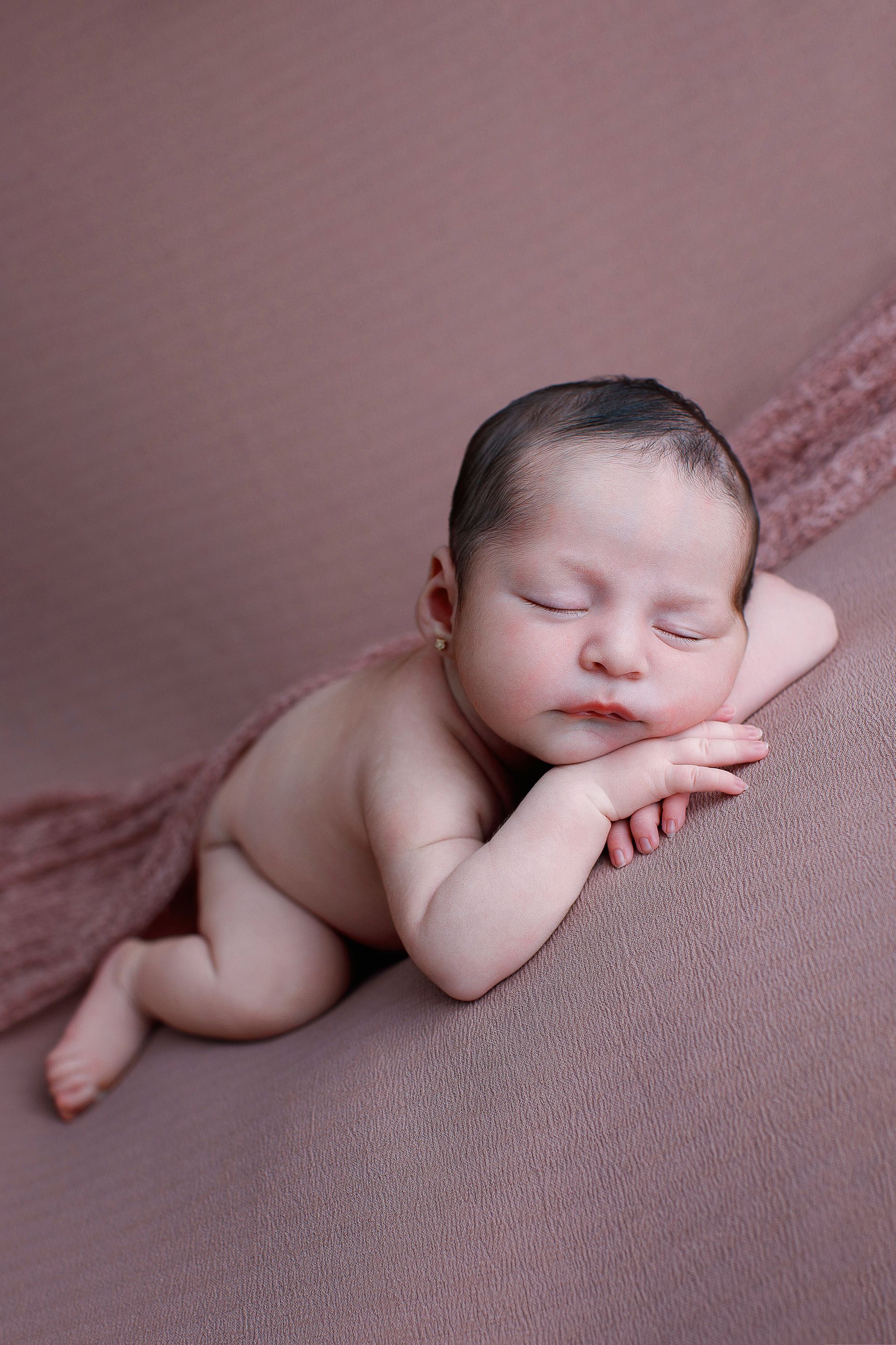 Un bebé recién nacido duerme sobre una manta rosa.