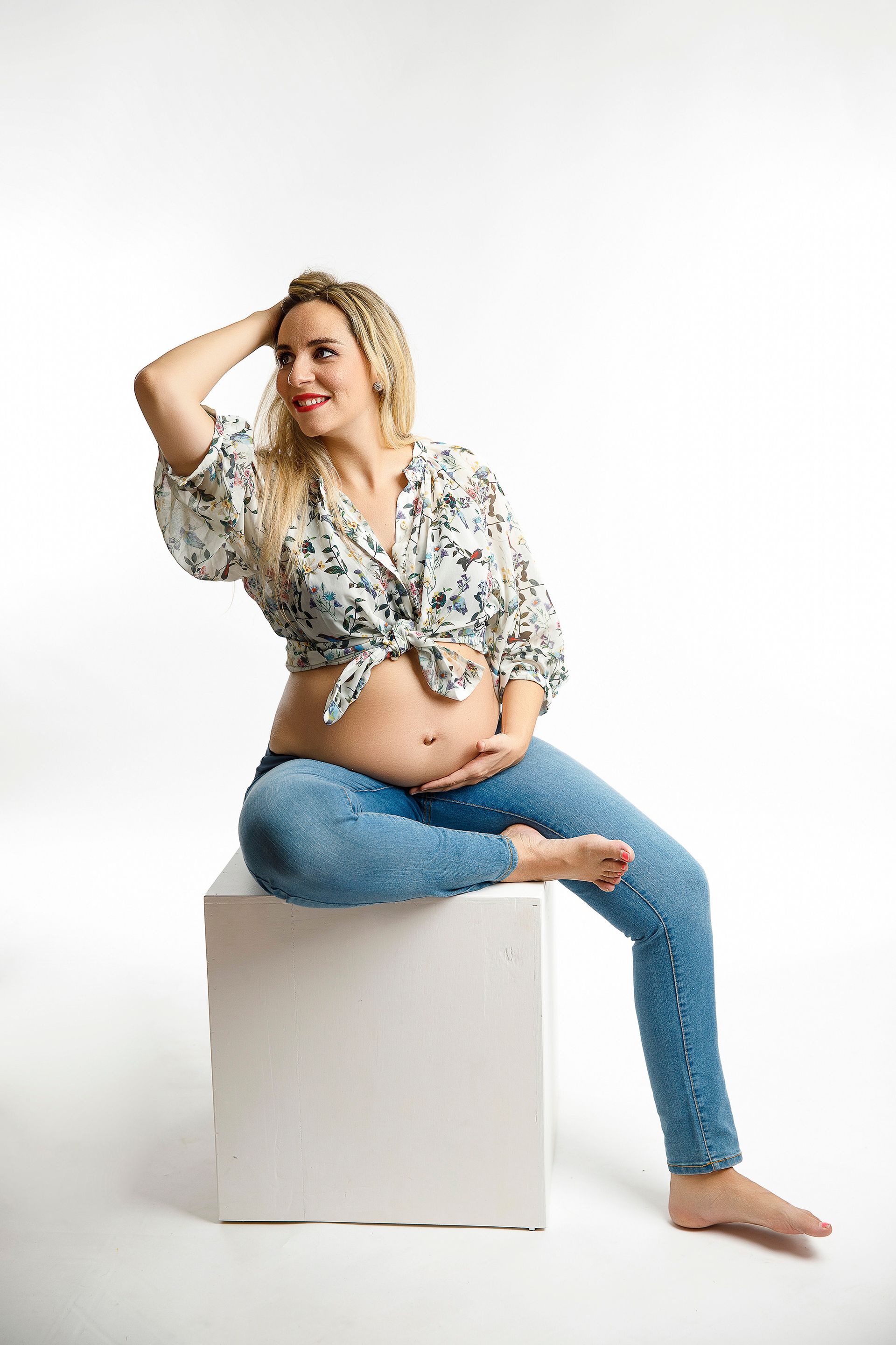 Una mujer embarazada está sentada en un cubo blanco.