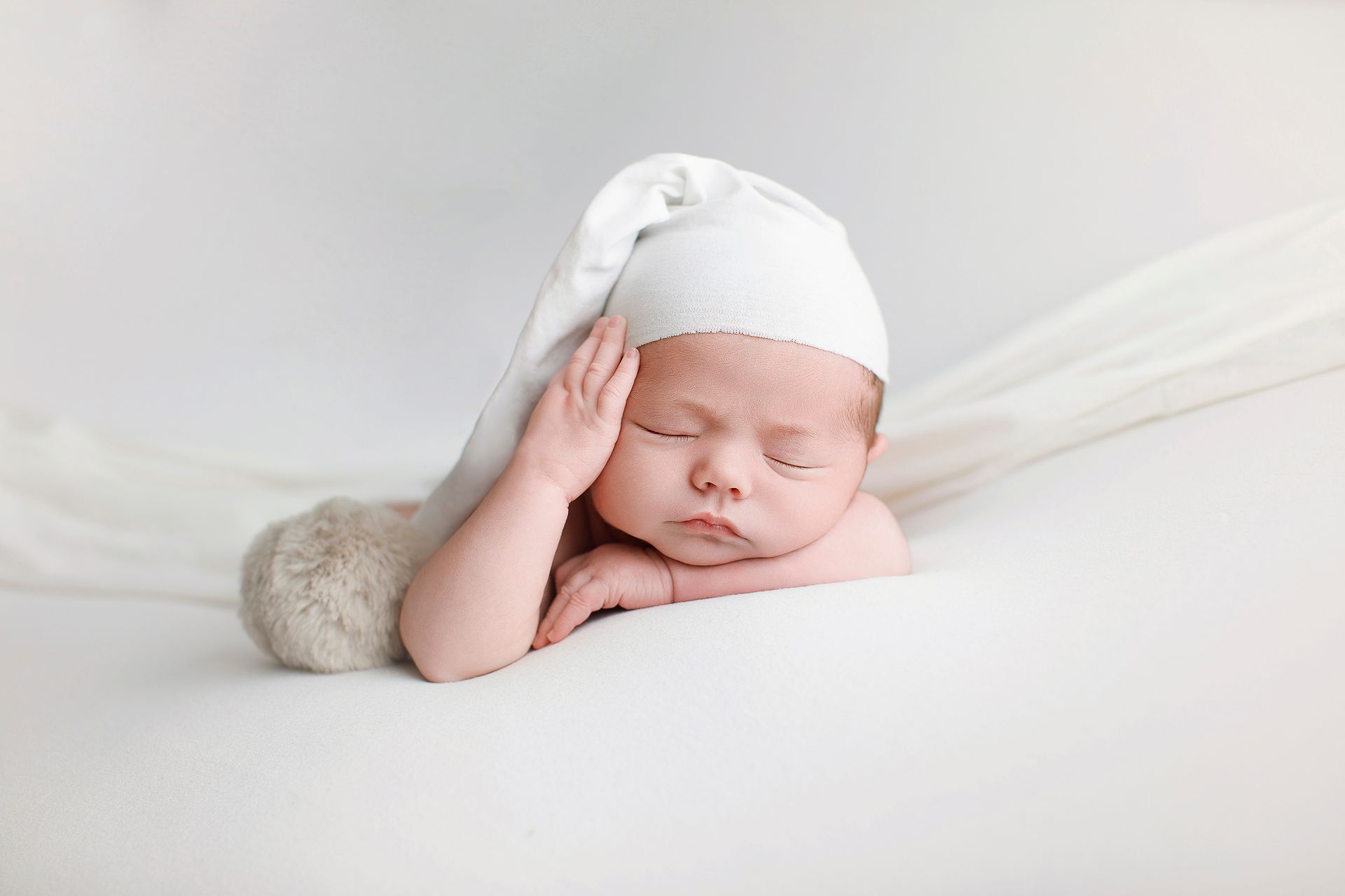 Un bebé recién nacido que lleva un sombrero blanco está durmiendo sobre una manta blanca.