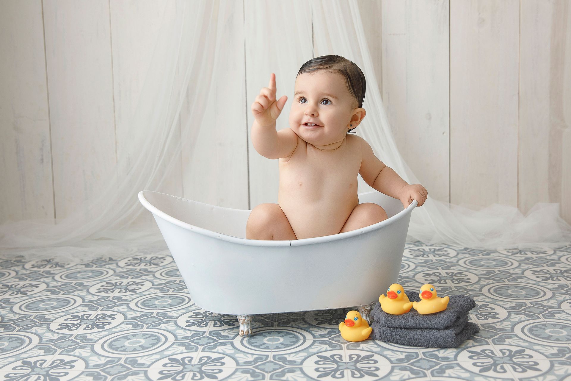 Un bebé está sentado en una bañera con patitos de goma y toallas.