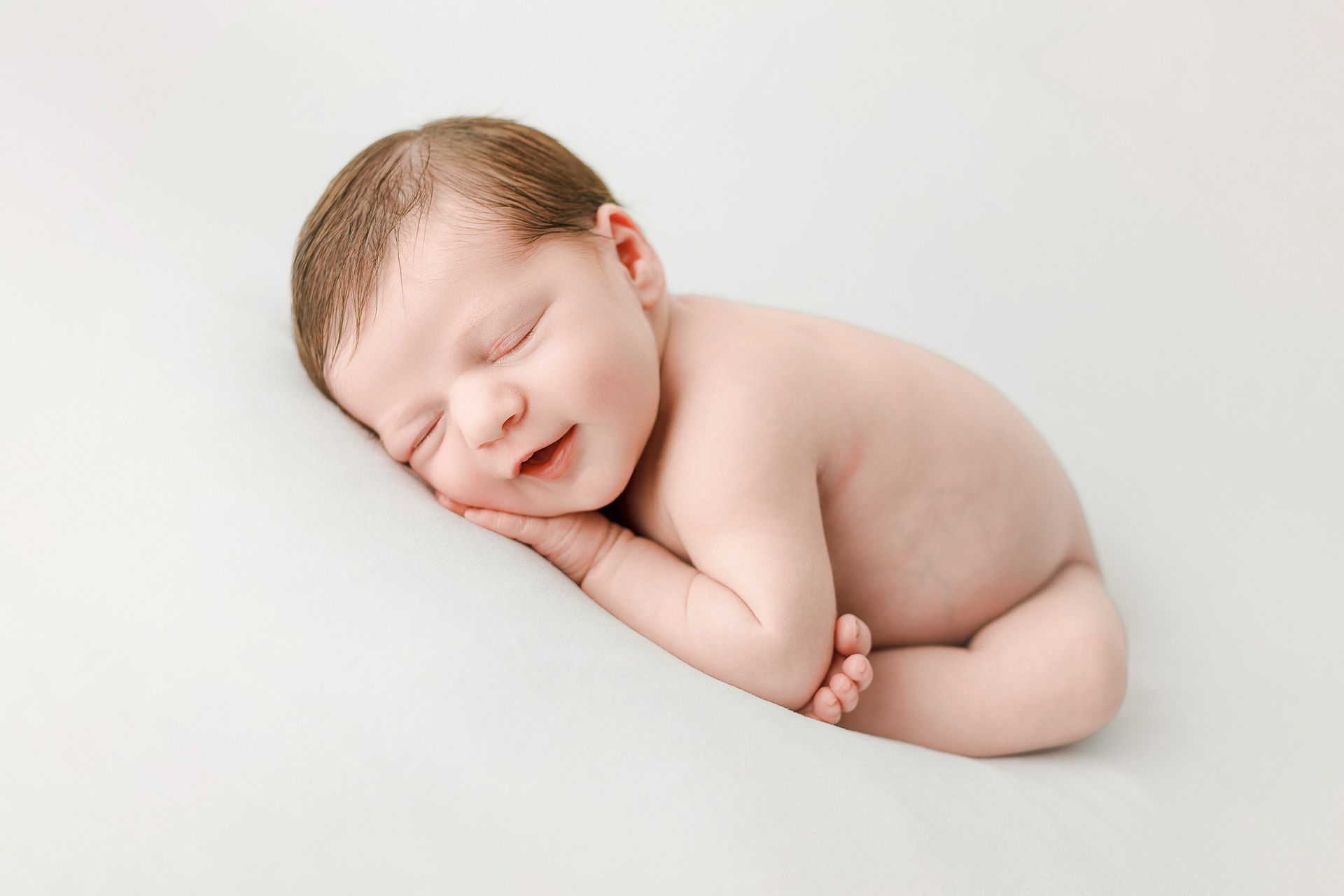 Un bebé recién nacido duerme sobre una manta blanca y sonríe.