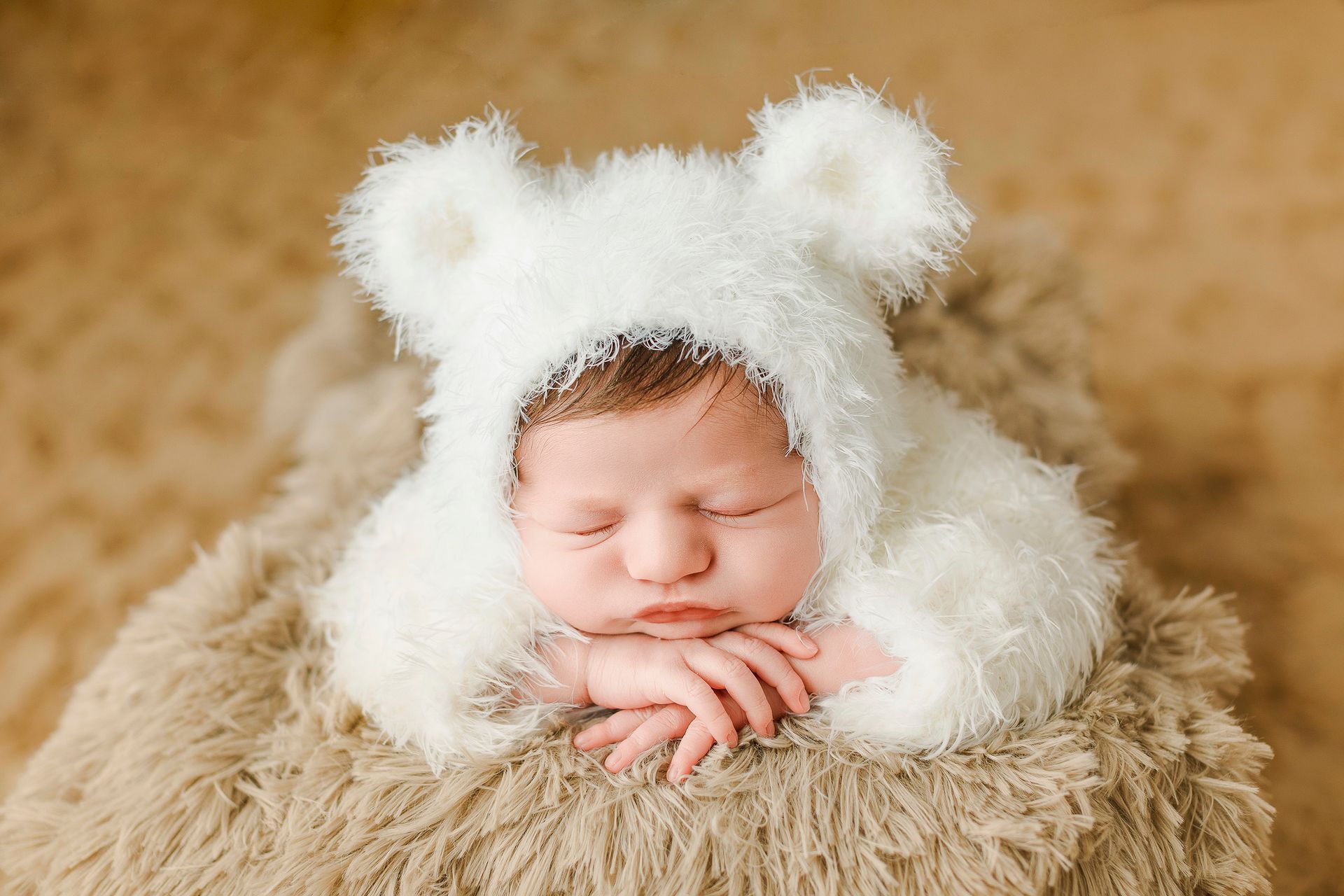 Un bebé recién nacido que lleva un gorro de osito de peluche blanco está durmiendo sobre una manta marrón.