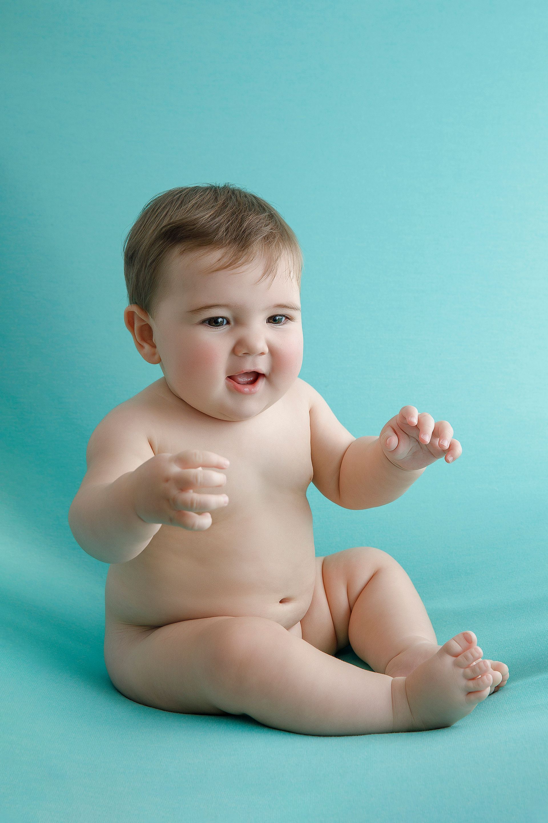 Un bebé está sentado sobre una manta azul y sonriendo.