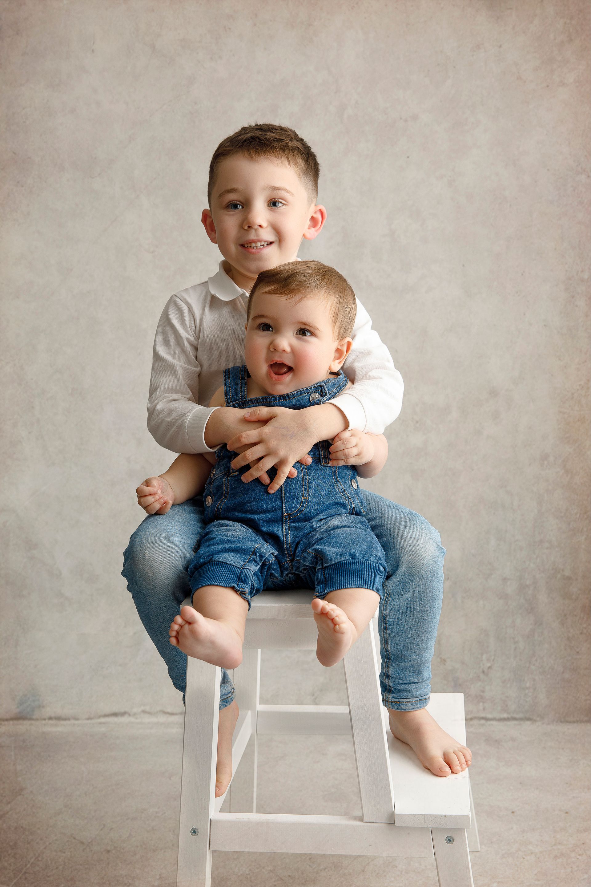 Un niño está sentado en un taburete sosteniendo un bebé.