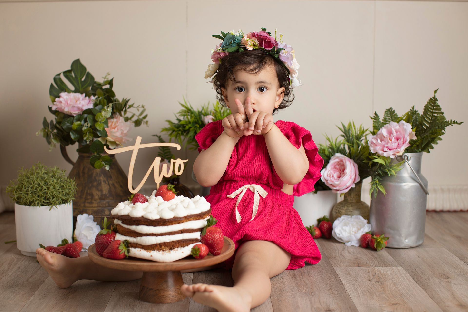 Una niña está sentada en el suelo al lado de un pastel.