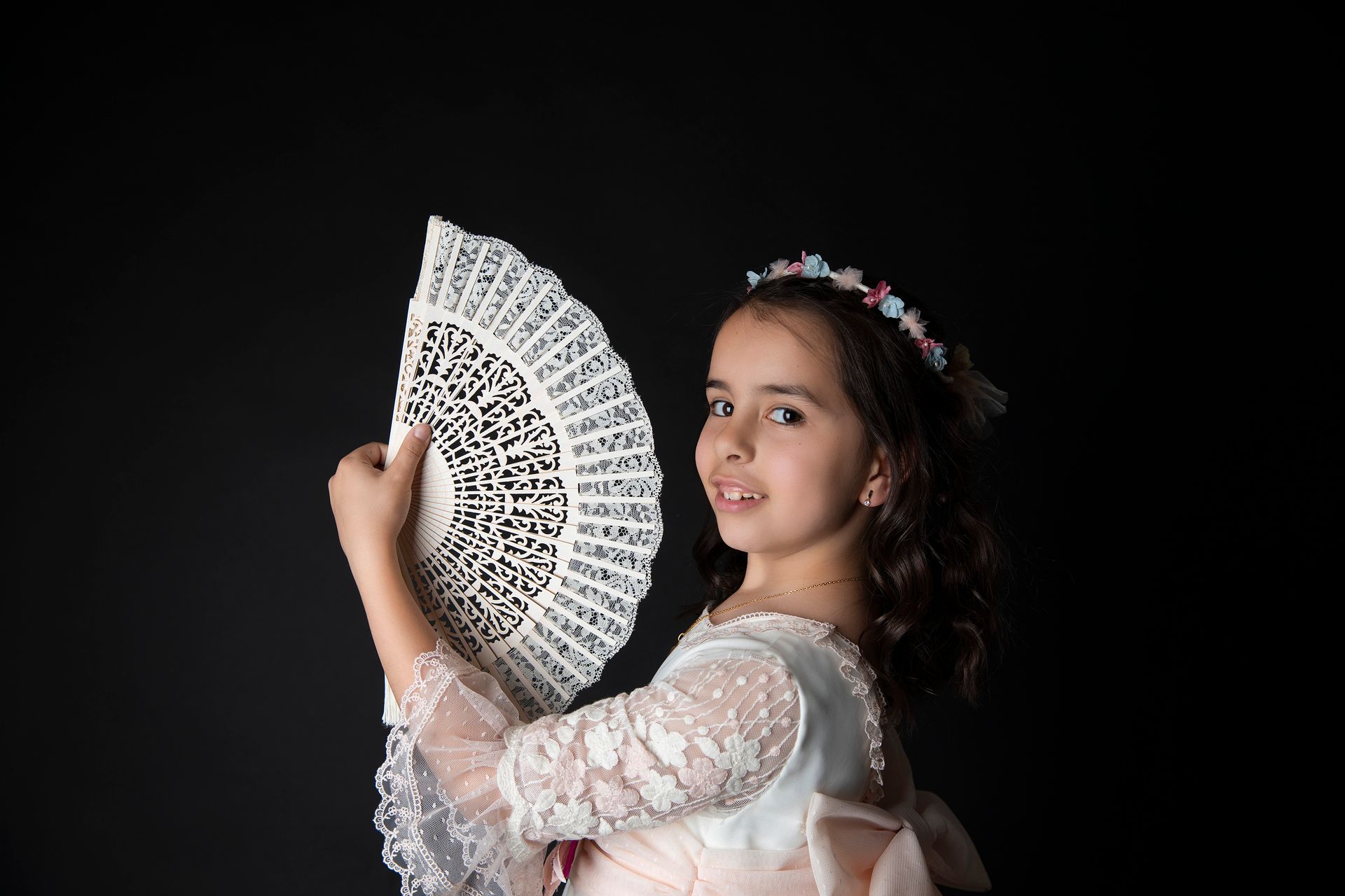 Una niña con un vestido rosa sostiene un abanico blanco.