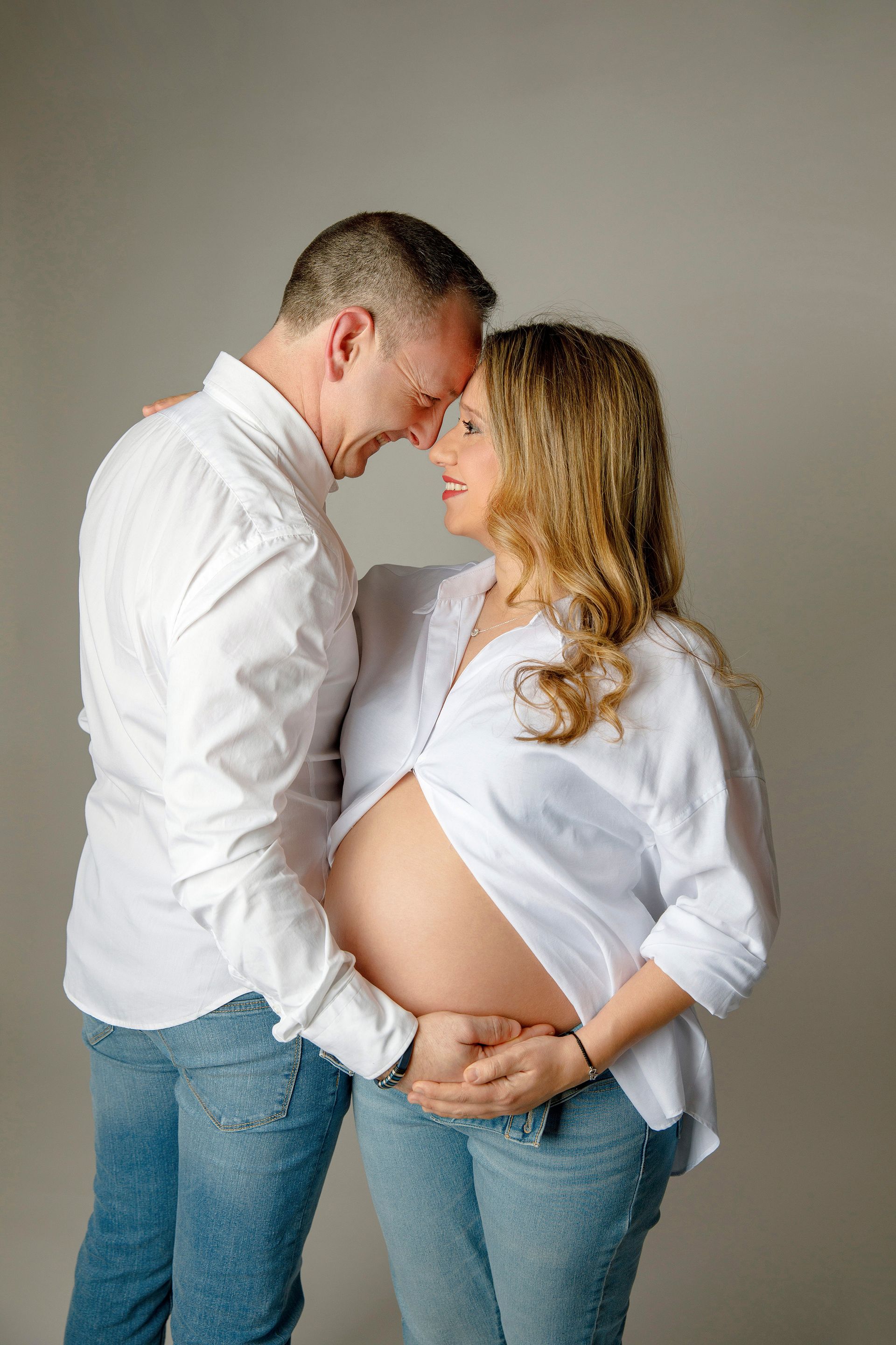 Un hombre y una mujer embarazada están parados uno al lado del otro y tocándose la frente.