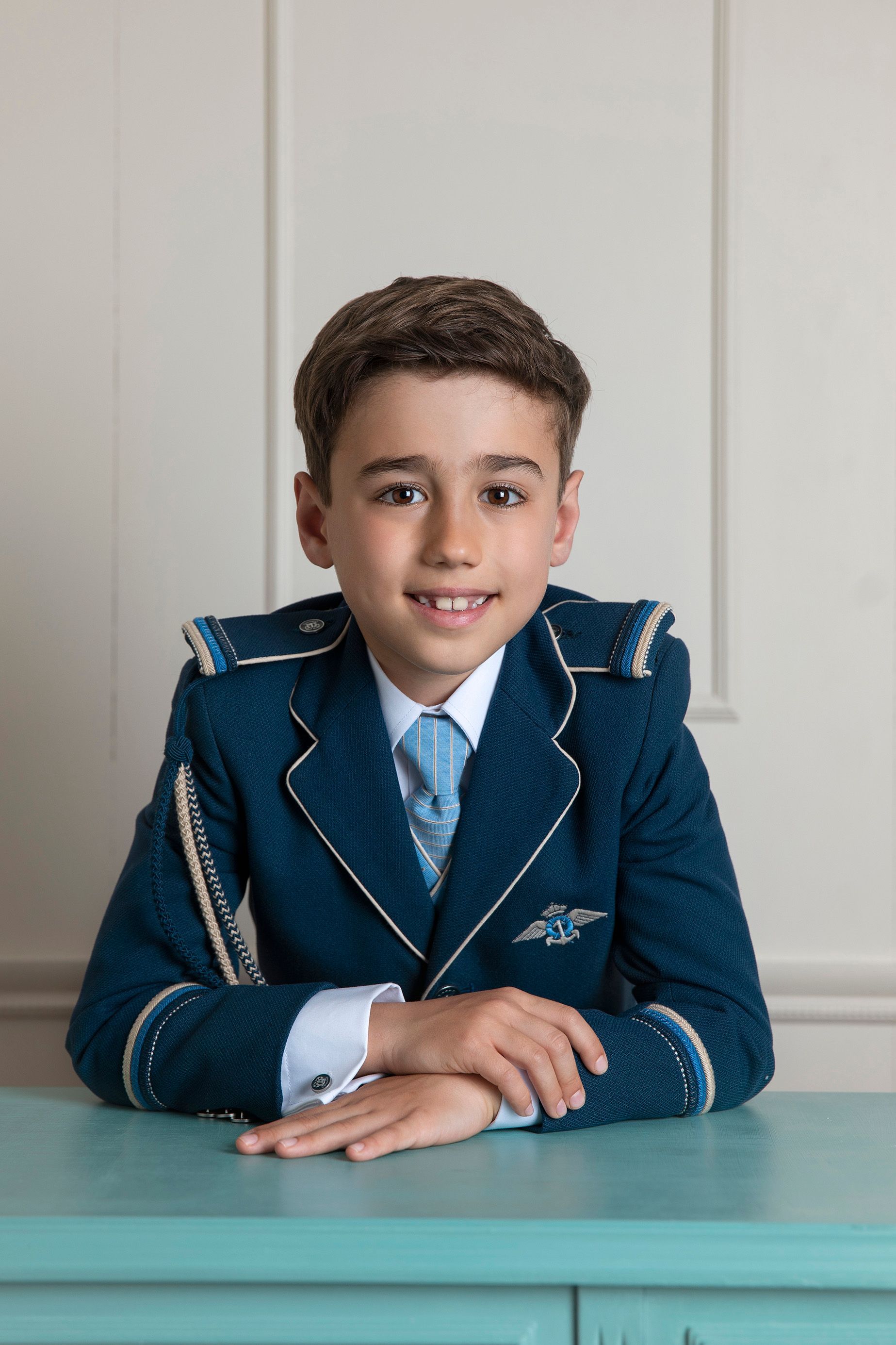 Un niño con traje azul y corbata está sentado en una mesa.