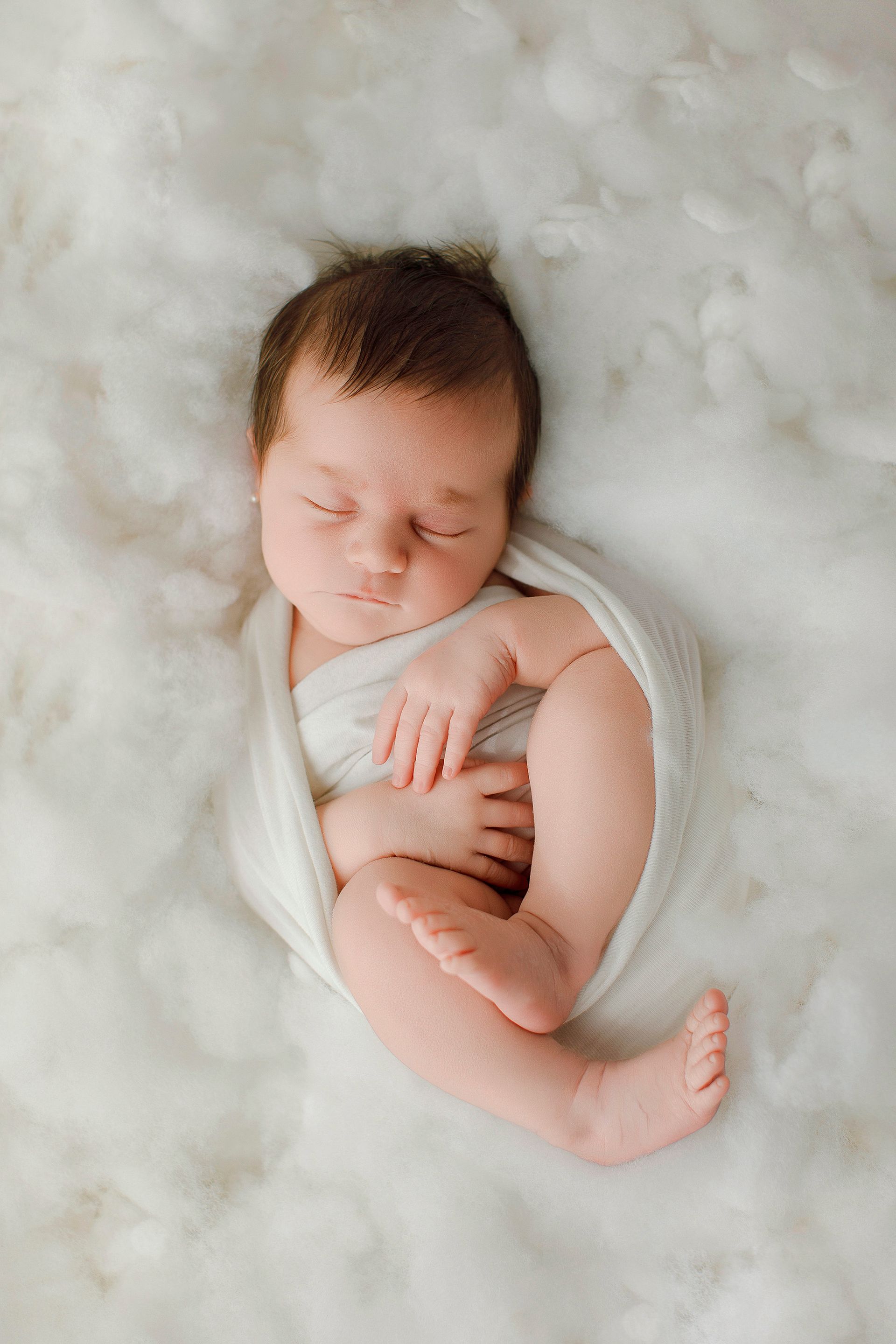 Un bebé recién nacido envuelto en una manta blanca está durmiendo sobre una manta blanca.