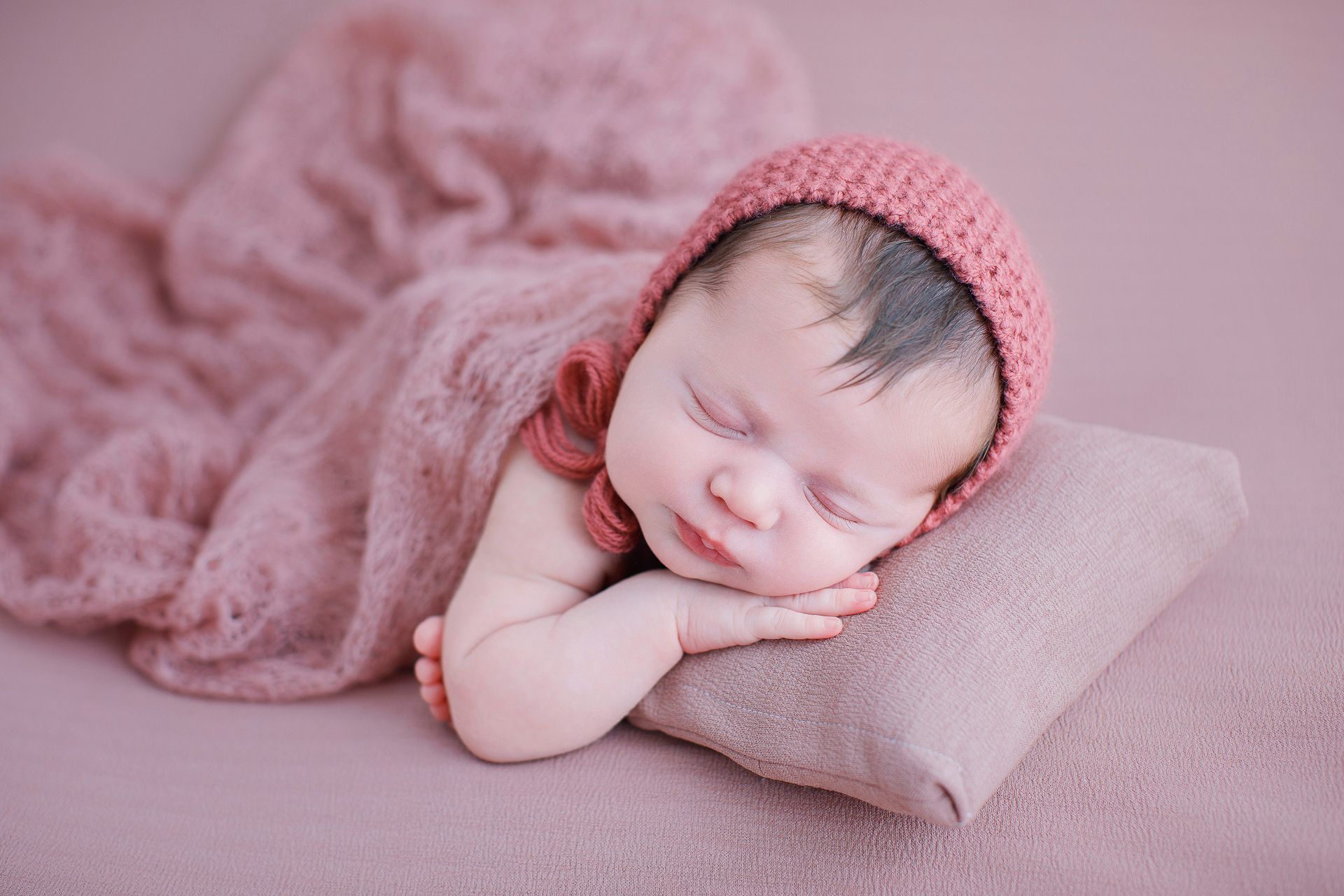 Un bebé recién nacido que lleva un sombrero rosa está durmiendo sobre una almohada.