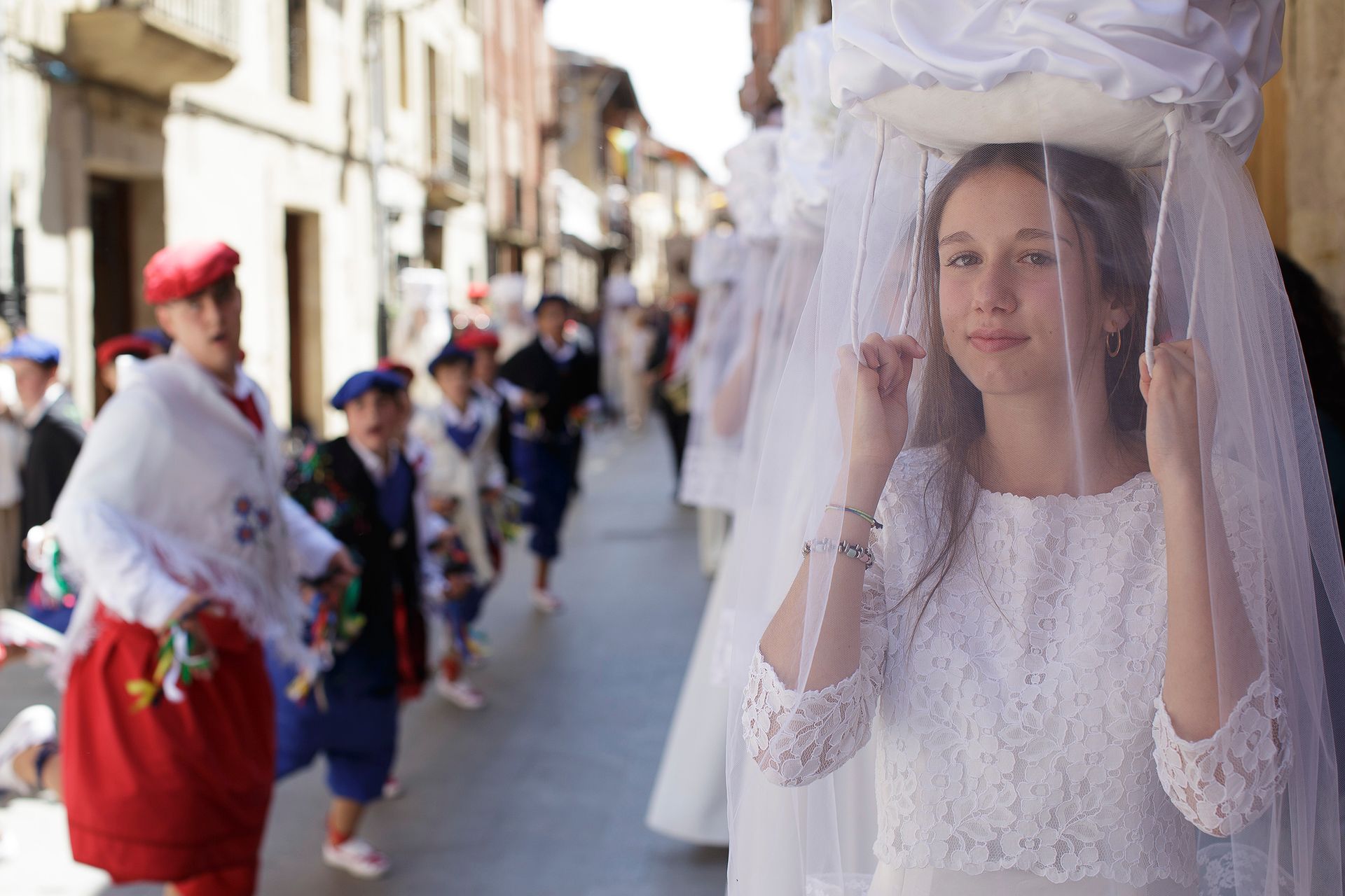 Una chica con un vestido de novia sostiene un velo sobre su cabeza.