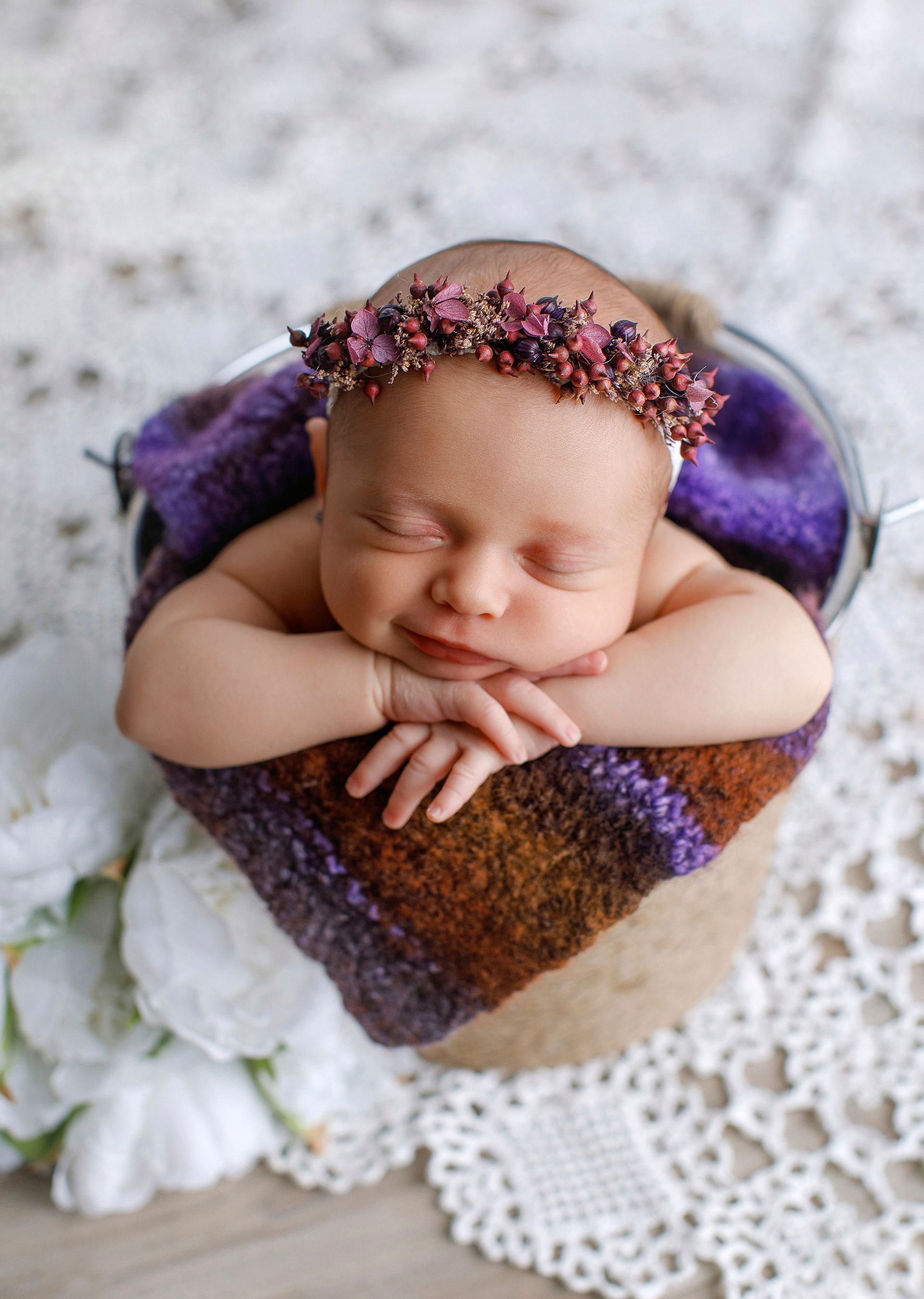 Un bebé recién nacido que lleva una corona de flores está durmiendo en un balde.