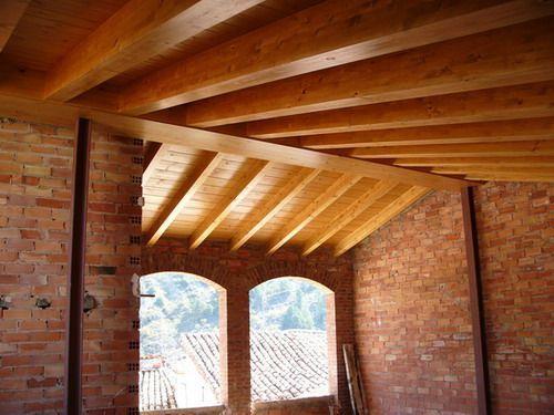 Interior de ladrillo visto con vigas de madera expuestas y una ventana que da a los tejados y las montañas.