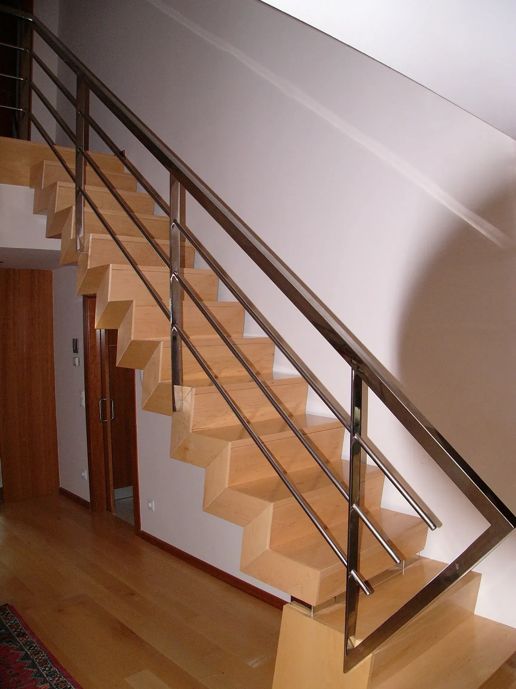 Escalera interior de madera con barandilla metálica y escalones de color claro a lo largo de una pared.