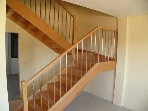Escalera interior de madera con paredes claras y barandillas blancas en el pasillo de una casa.