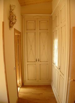 Pasillo estrecho y soleado con armarios empotrados blancos y suelo de madera en un interior beige.
