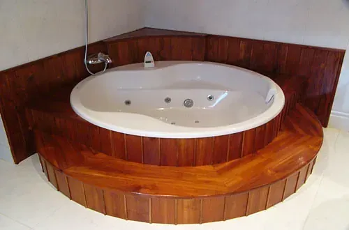 Bañera ovalada con marco de madera en un rincón de baño alicatado.