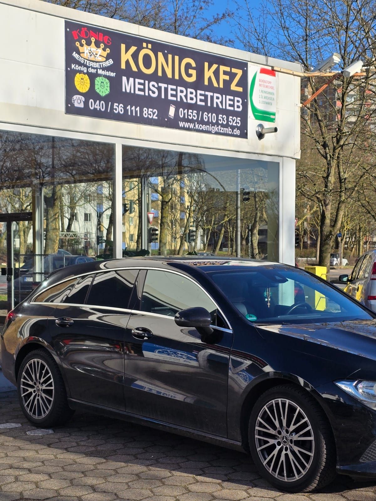 Ein schwarzes Auto parkt vor einem Schild mit der Aufschrift „König Kfz Meisterbetrieb“