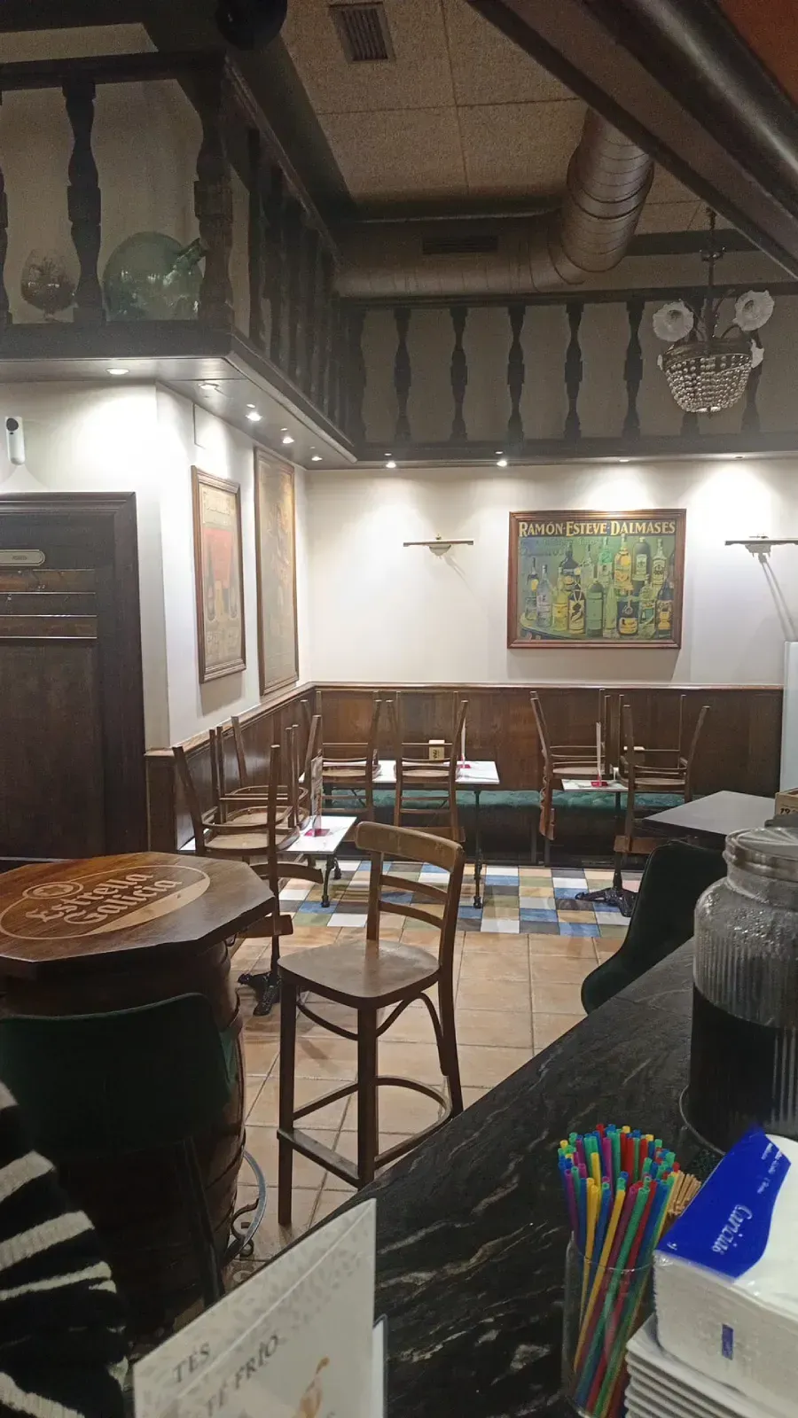 Un cartel amarillo y negro de Estrella Galicia cuelga sobre un edificio de paredes de ladrillo y grandes ventanales.