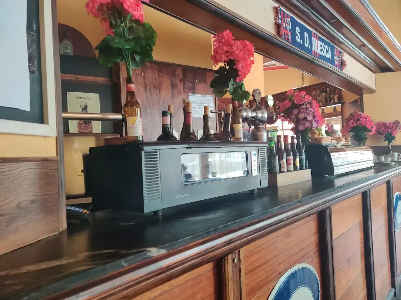 Una barra de bar de madera con una vitrina para calentar vasos, botellas y flores rosas decorativas