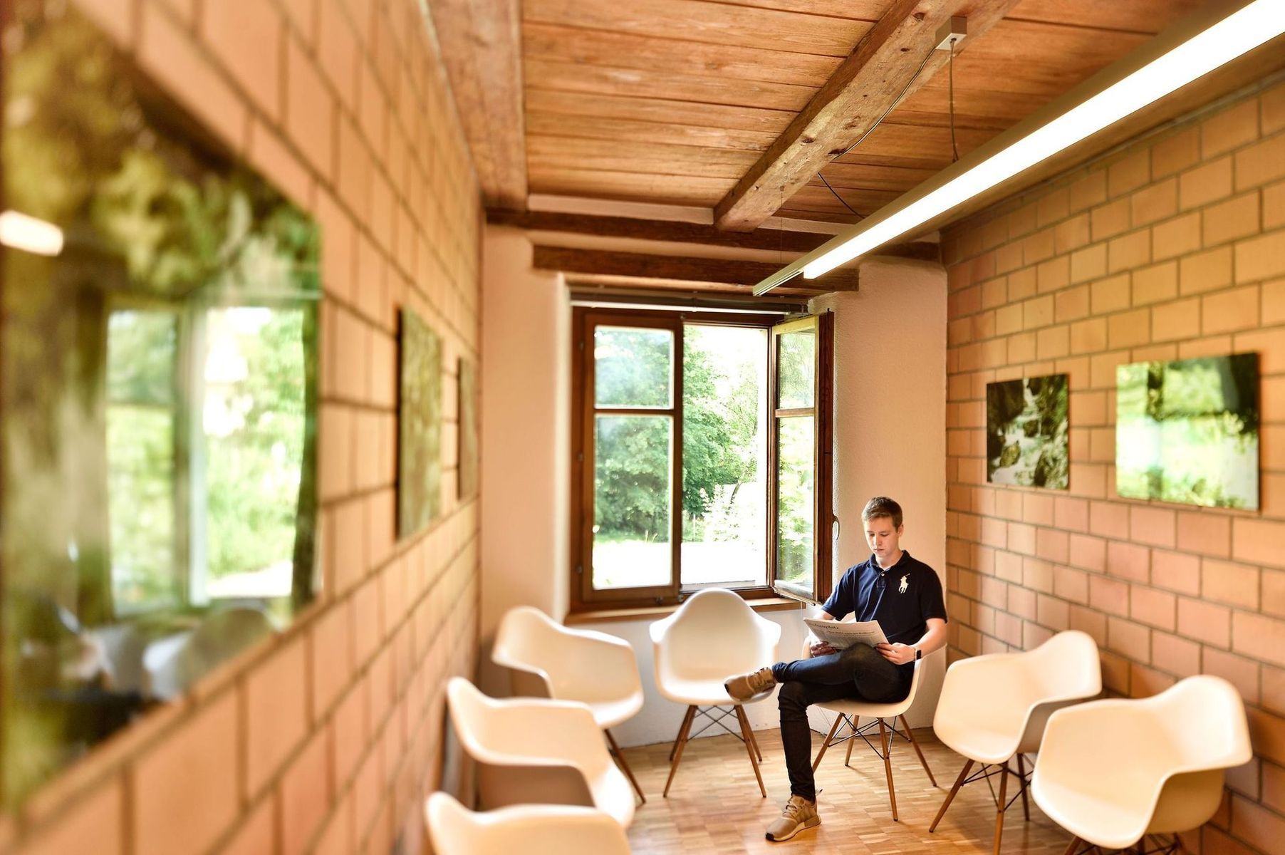 Moderne Lounge mit weissen Stühlen, Holzwänden und einer Person, die an einem Fenster sitzt.