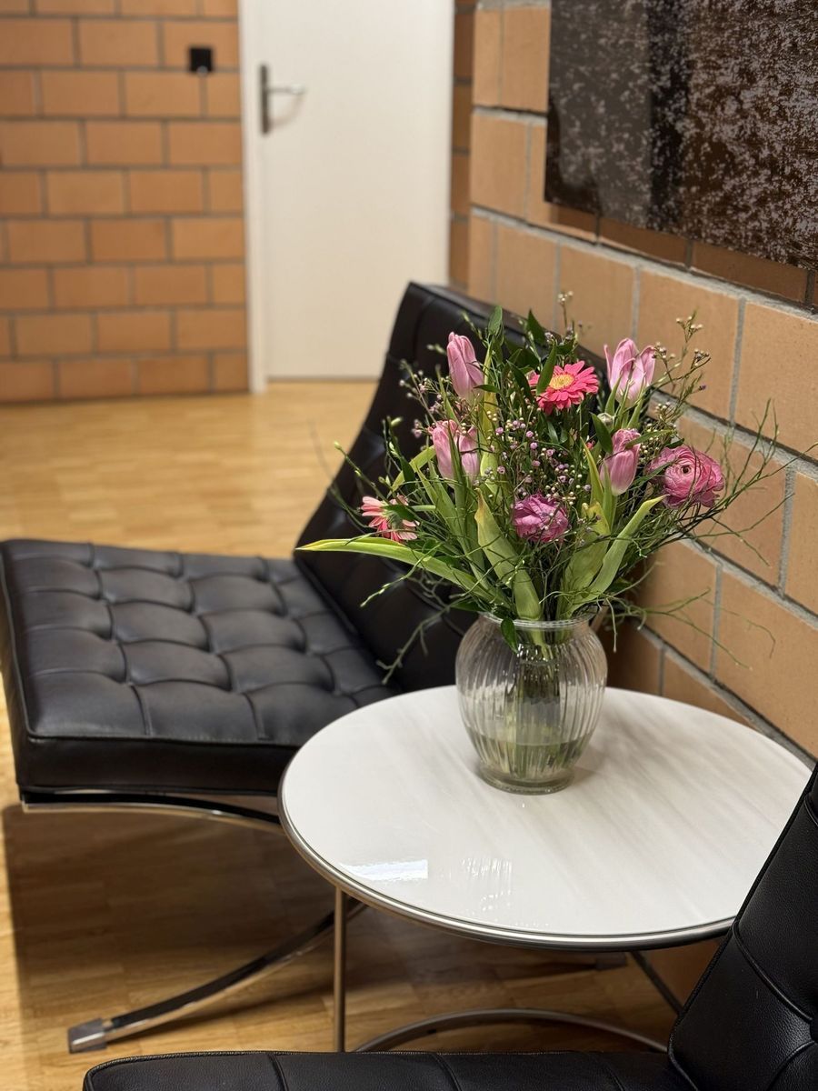Kleiner runder weisser Tisch mit einer Vase mit rosa Blumen neben einem schwarzen gepolsterten Stuhl in einem Flur.