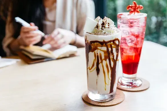 Una mujer escribe en un cuaderno mientras está sentada en una mesa con dos bebidas.
